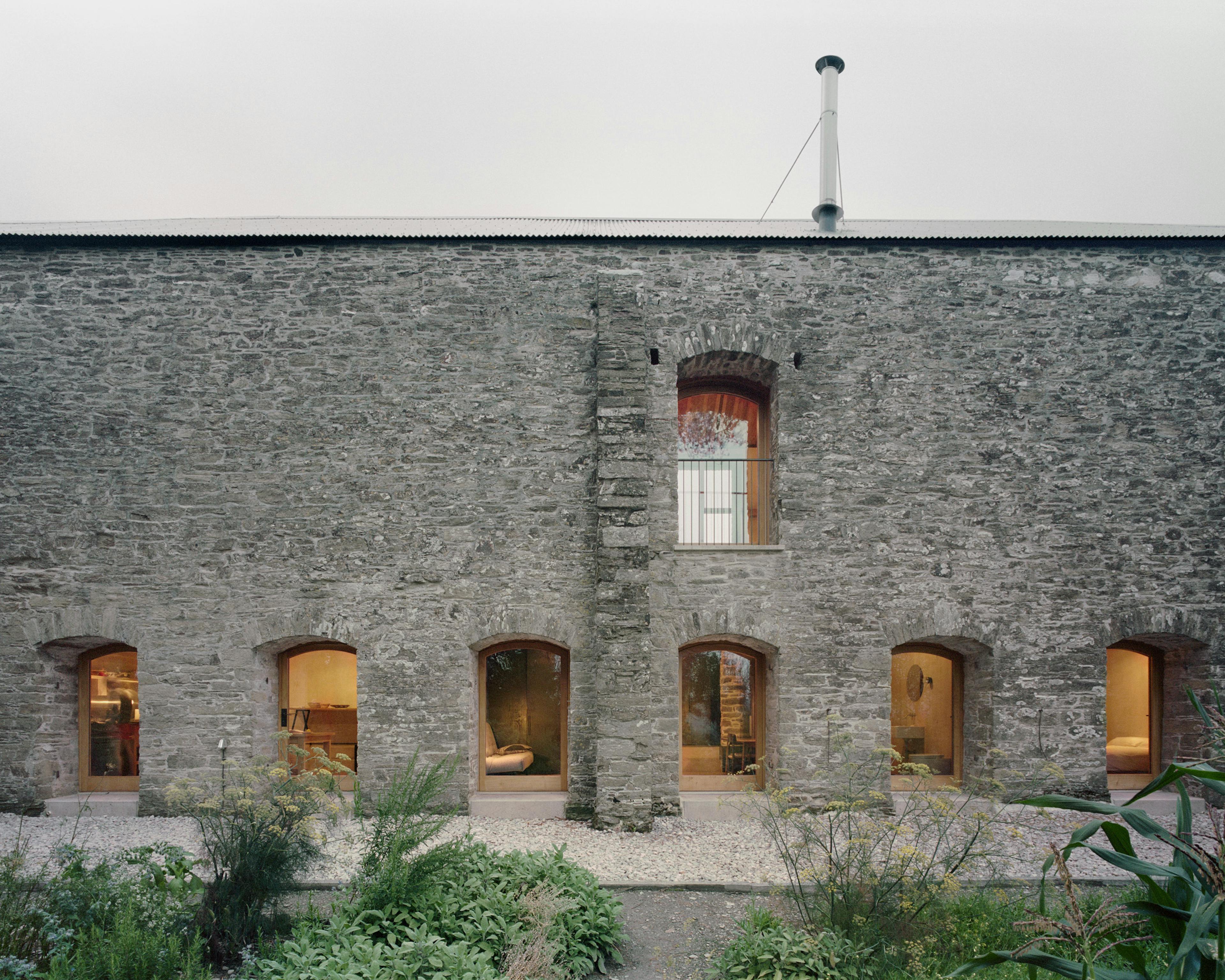 Lights shine from windows of a renovated stone barn at dusk