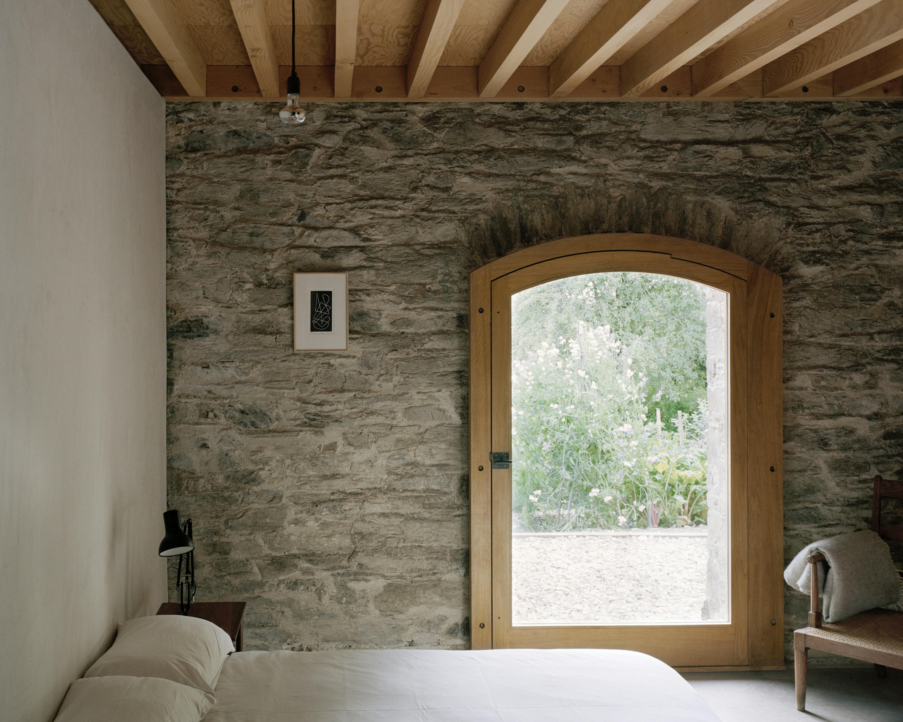 A bedroom with a wooden glazed door in a renovated stone barn with a Douglas fir frame