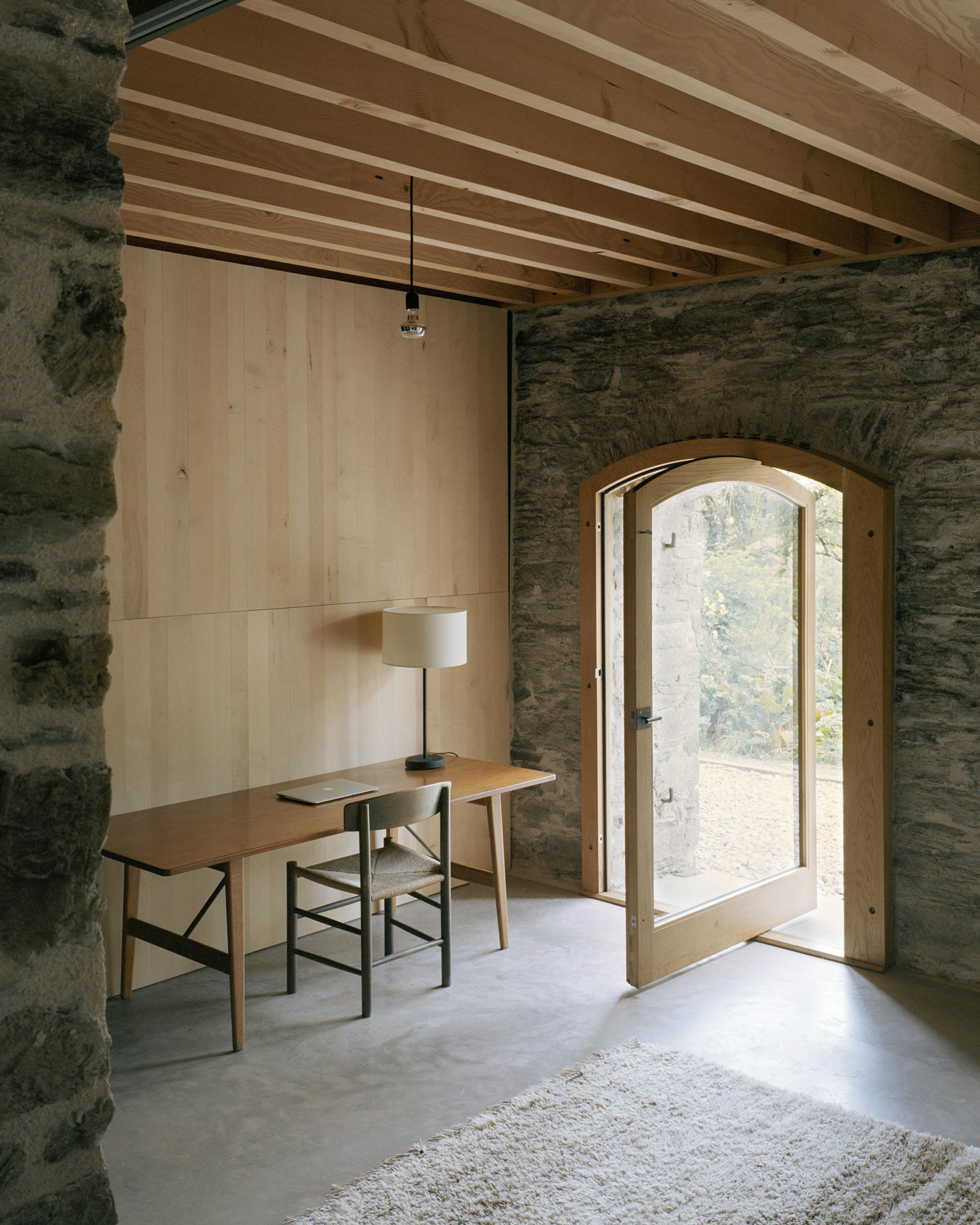 A study area next to an open wooden glazed door of a renovated stone barn with a Douglas fir frame