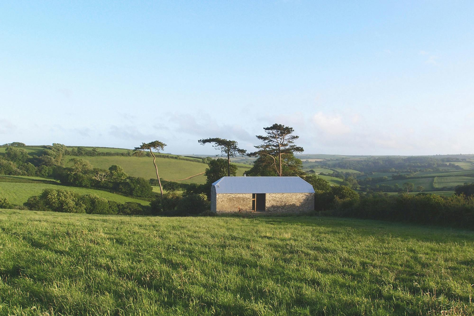 A renovated stone barn at dusk in a green field with blue skies behind