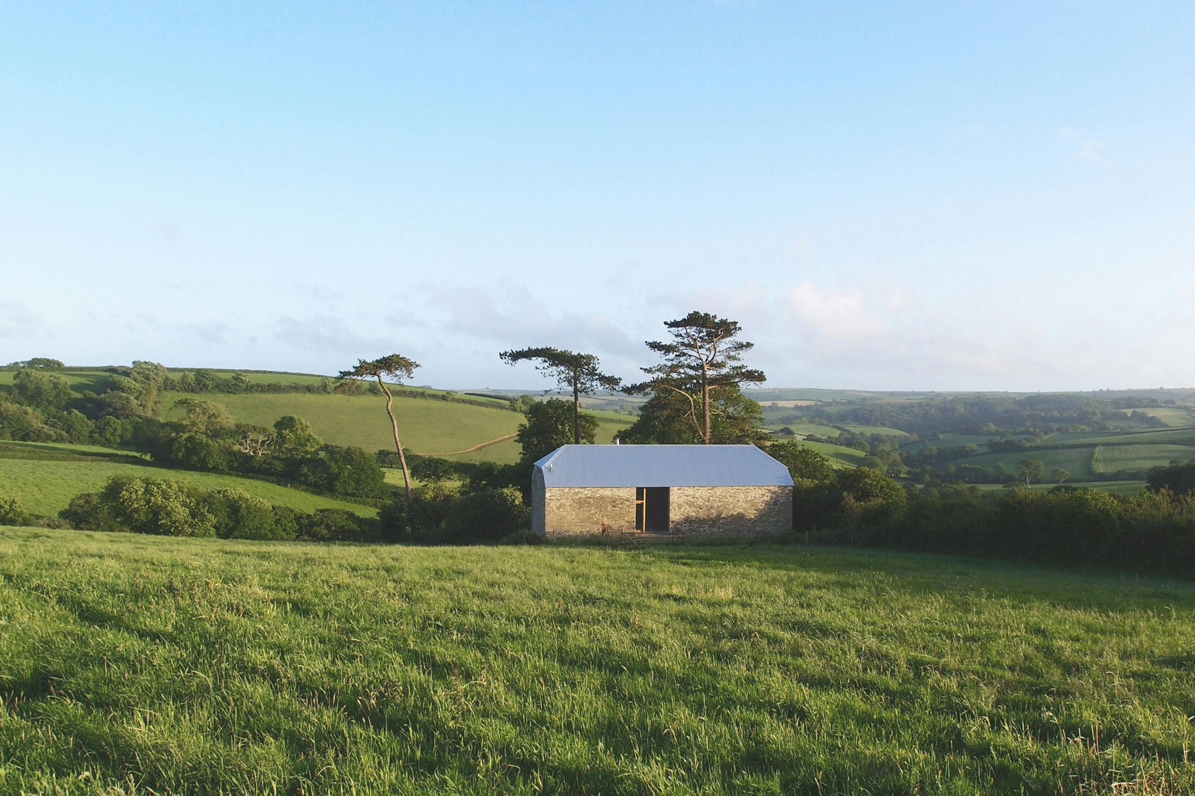 A renovated stone barn at dusk in a green field with blue skies behind