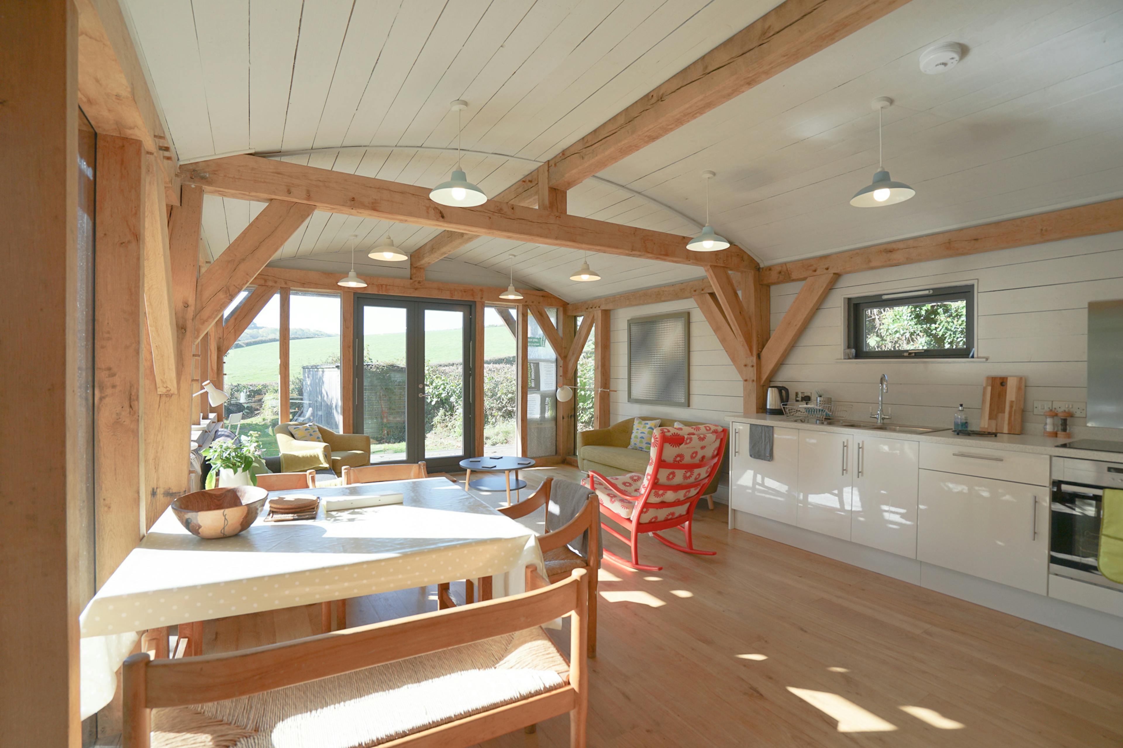 The open plan living, dining, sitting room of an oak framed cabin with a curved white painted roof