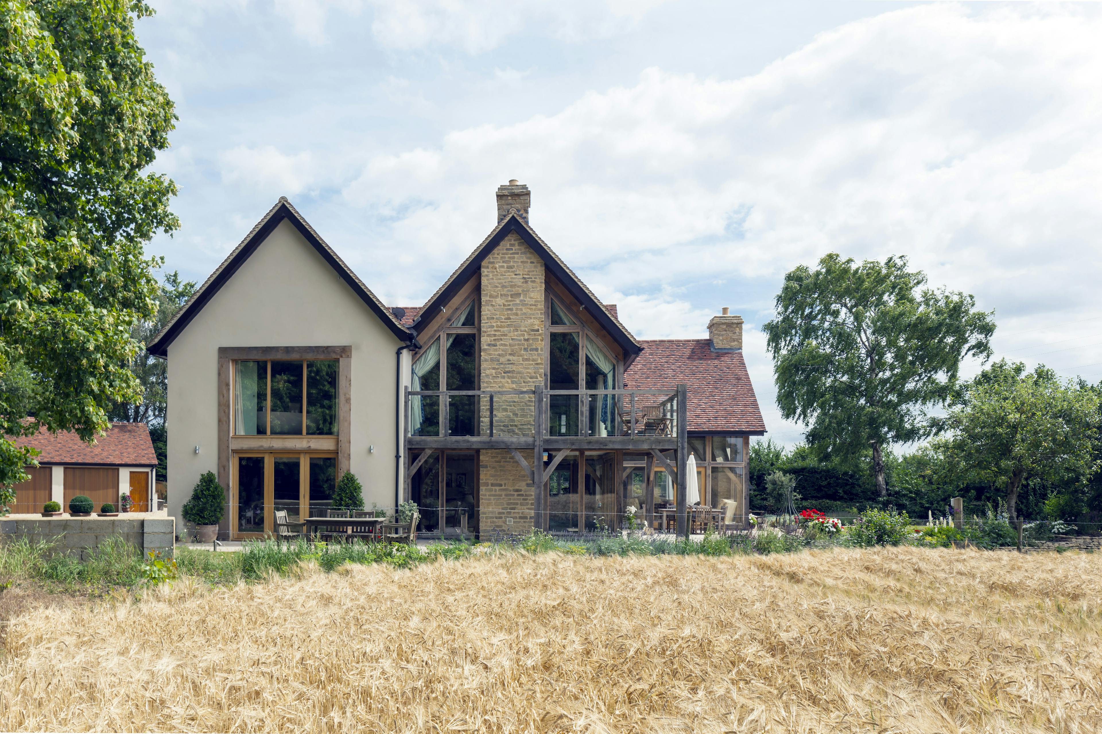 The rear of an oak framed home with oak balconies next to a yellow field
