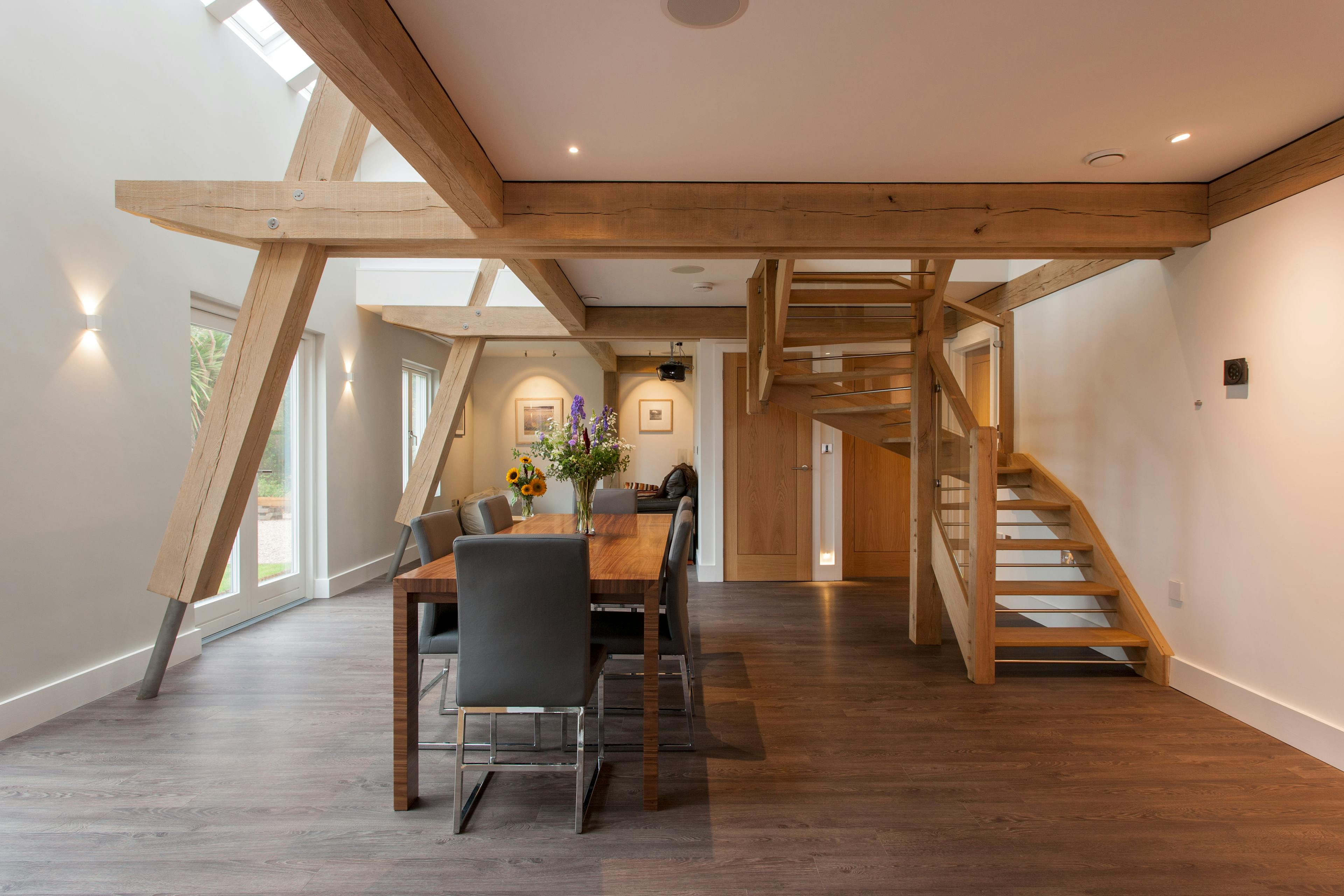 A dining area in a modern oak and steel framed home with a wooden staircase