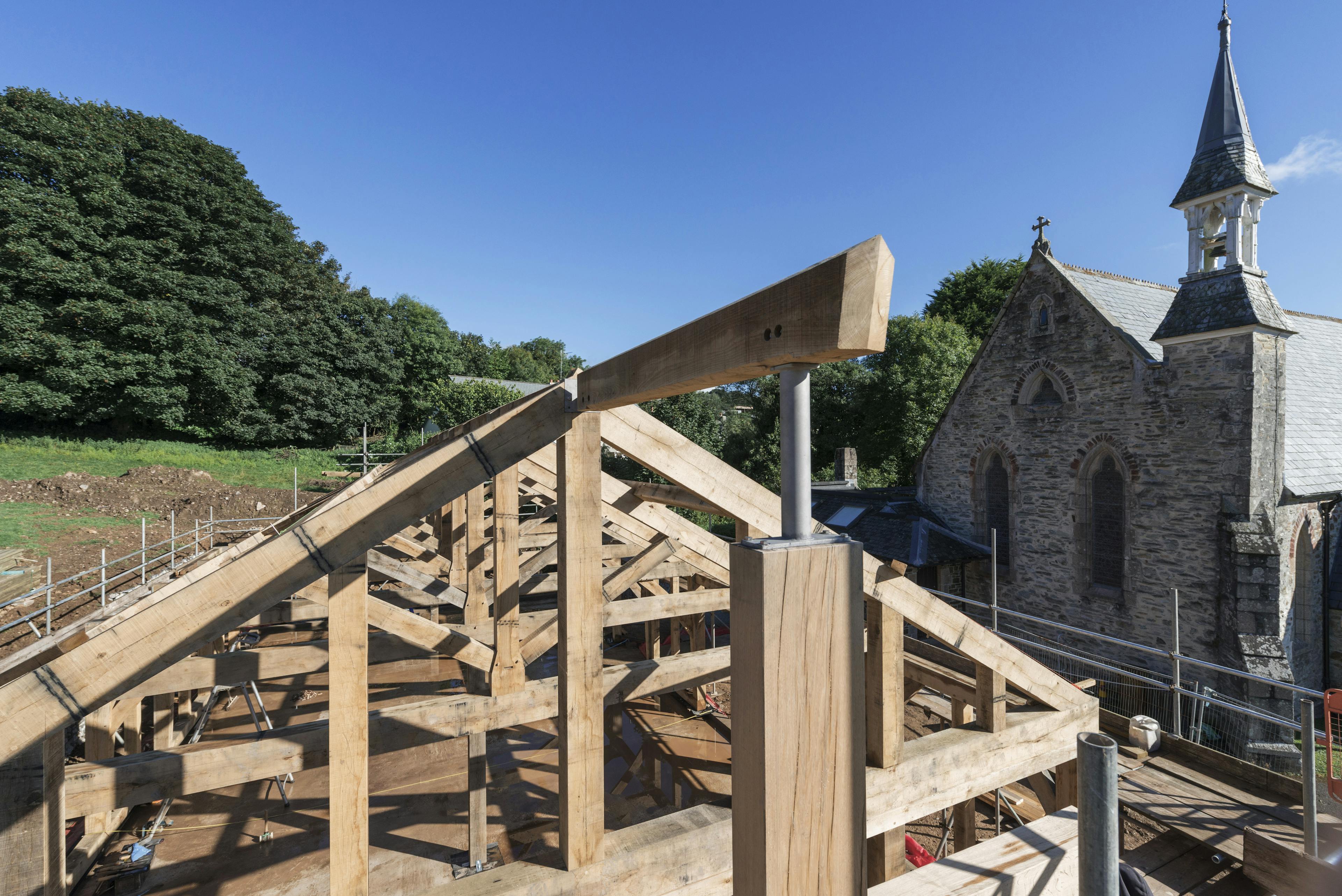 An oak frame during construction with a church behind it