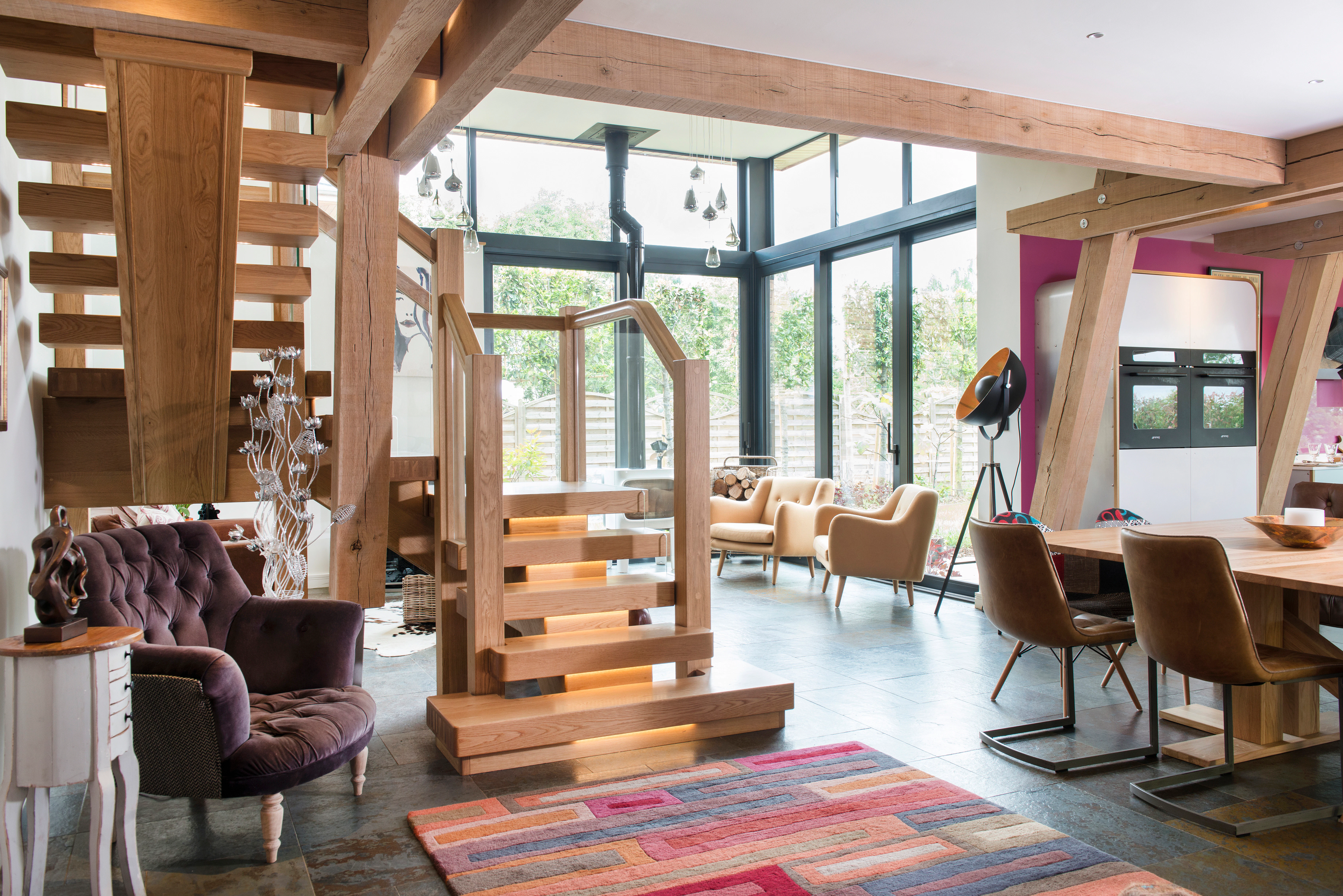 An open plan oak framed living room with dining and sitting areas and wooden stairs