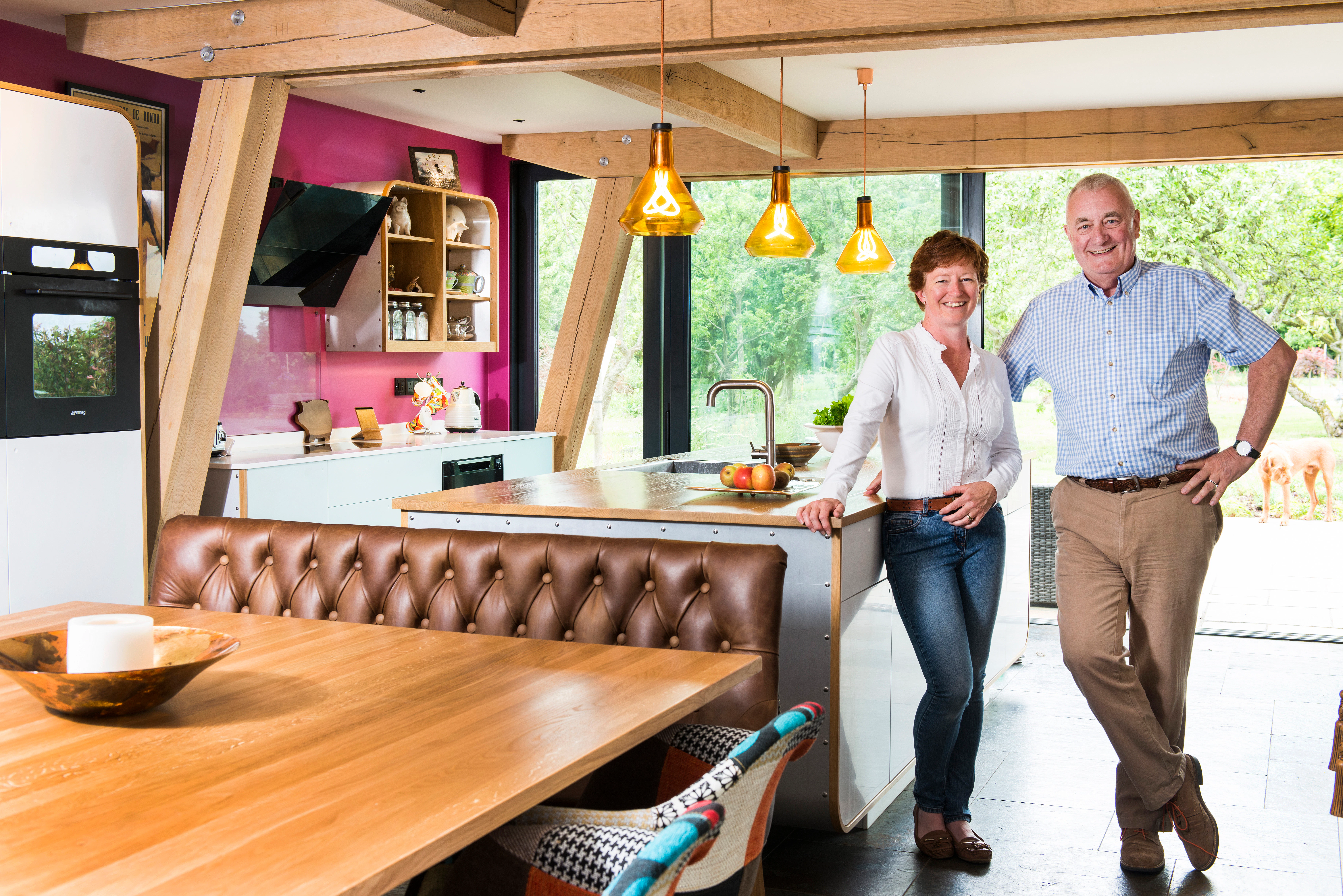 A man and a woman stand in their open plan oak framed kitchen and dining area