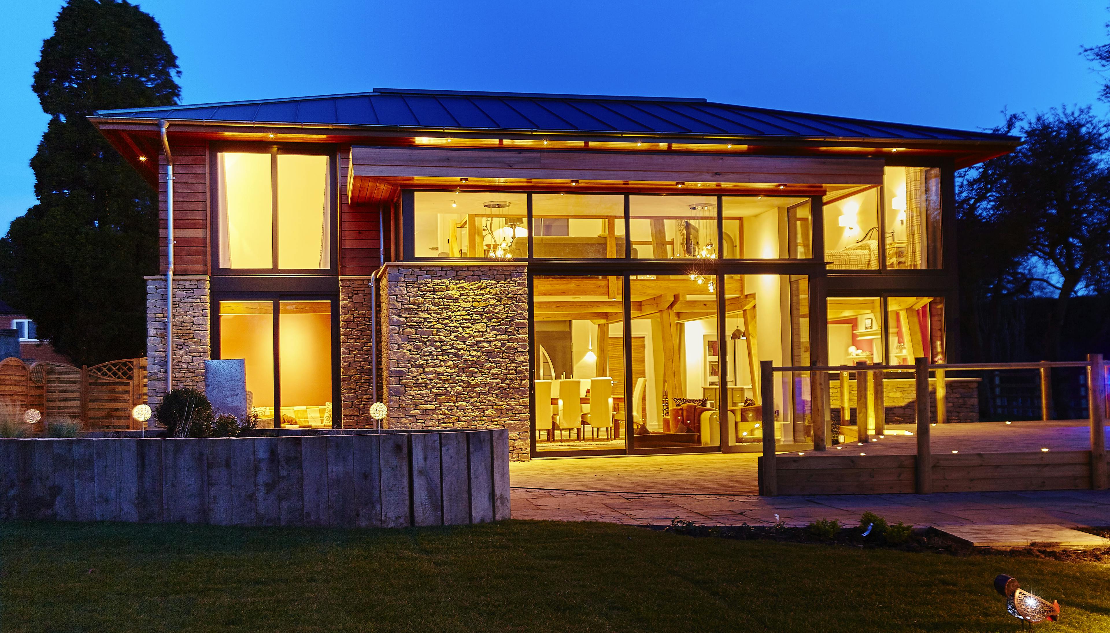 At dusk light shines from the windows of a modern two storey oak framed home with glazing
