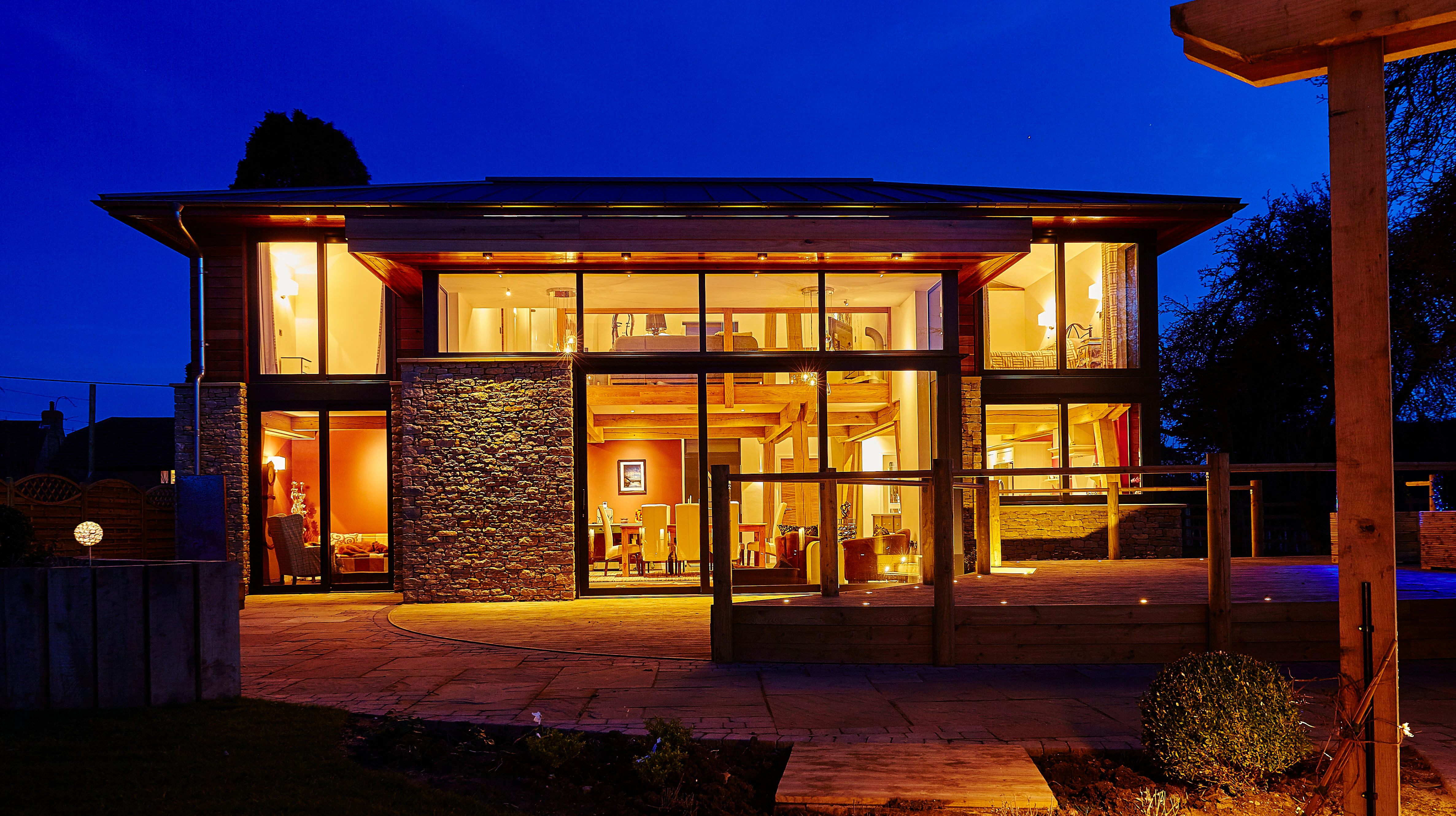 At dusk light shines from the windows of a modern two storey oak framed home with glazing