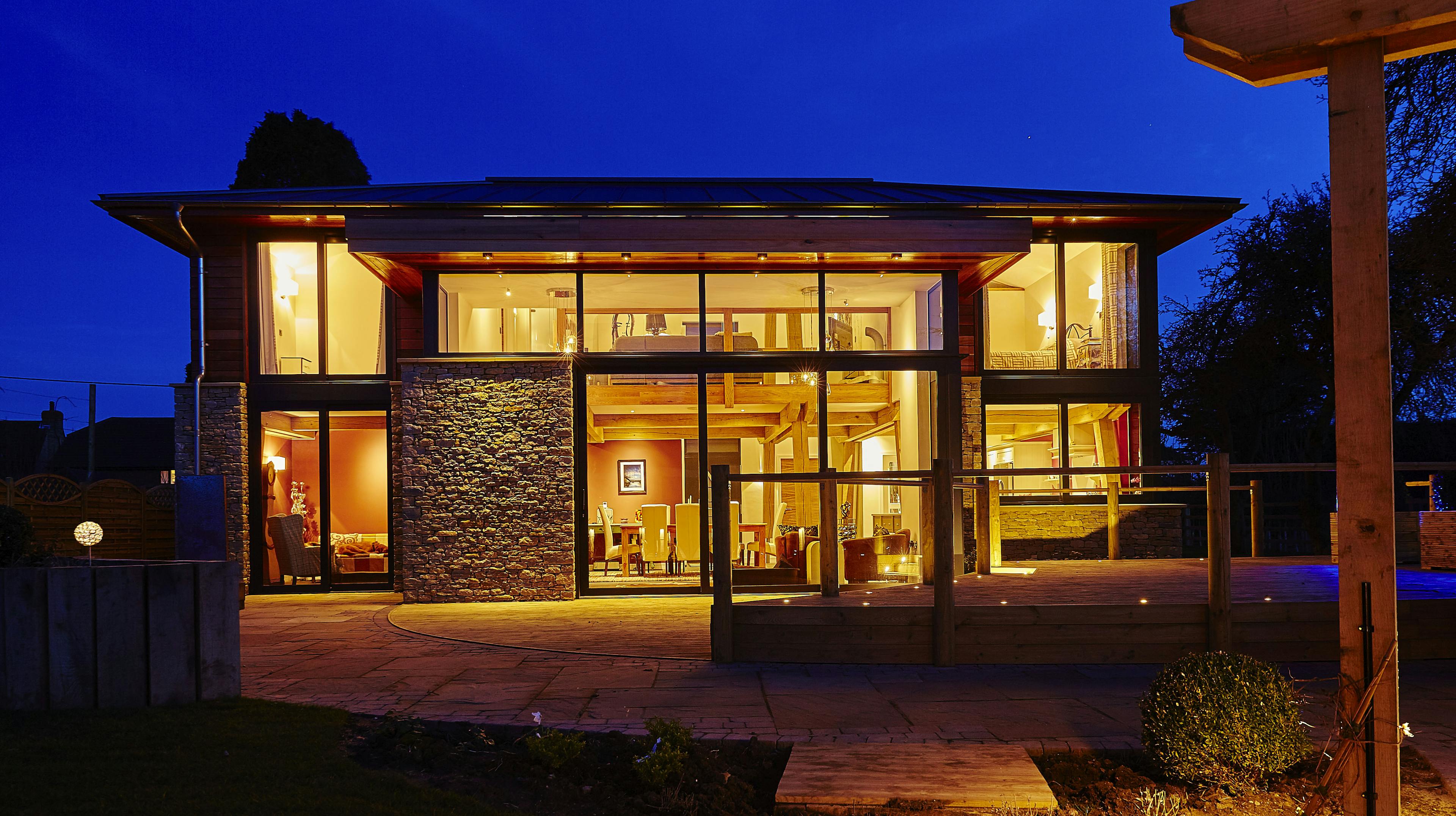 At dusk light shines from the windows of a modern two storey oak framed home with glazing