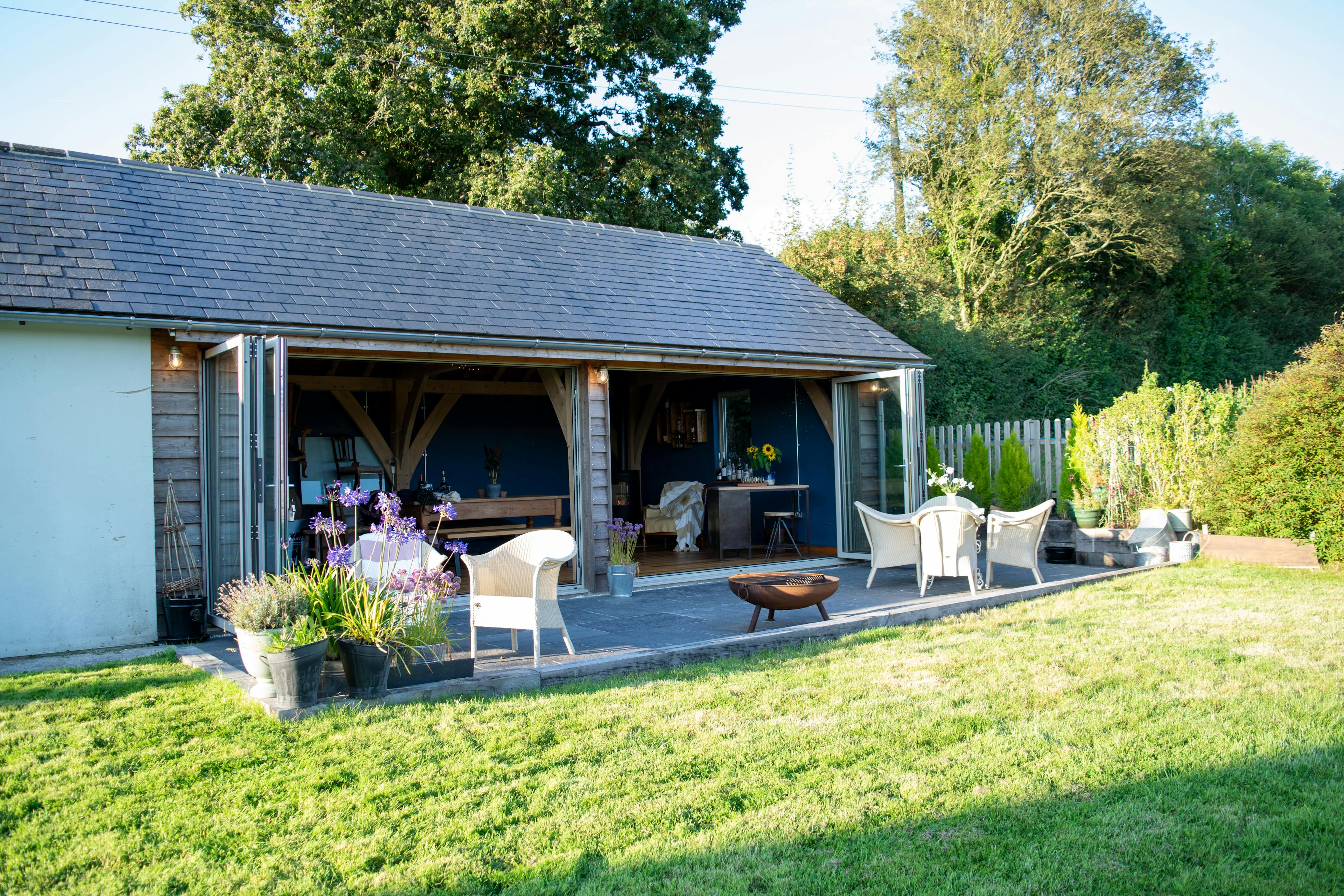 A 2-bay oak framed extension with bi-fold doors opening out to a garden with outdoor seating and a green lawn