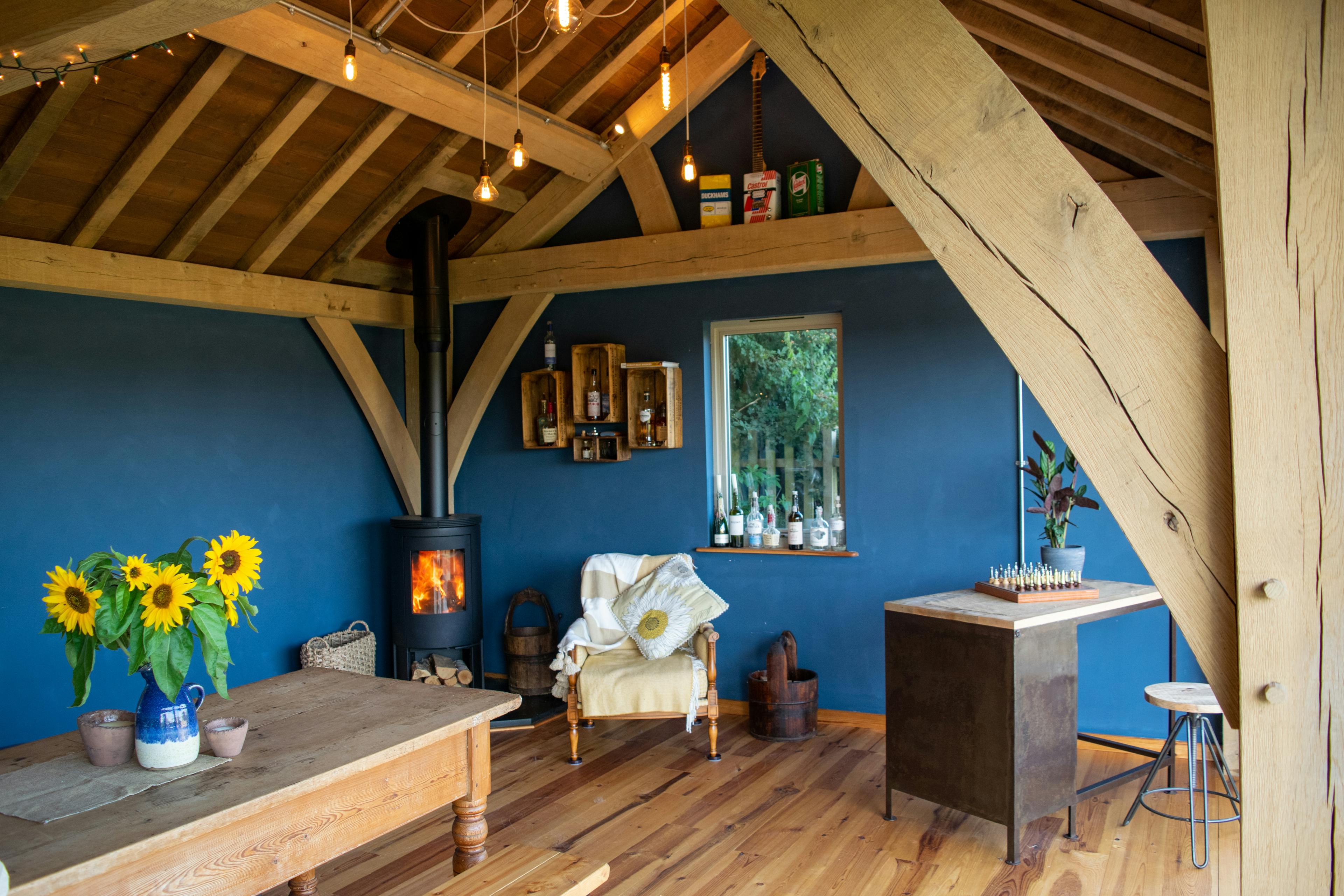 The inside of a 2-bay oak framed extension with a log burner and bi fold doors opening out to a garden