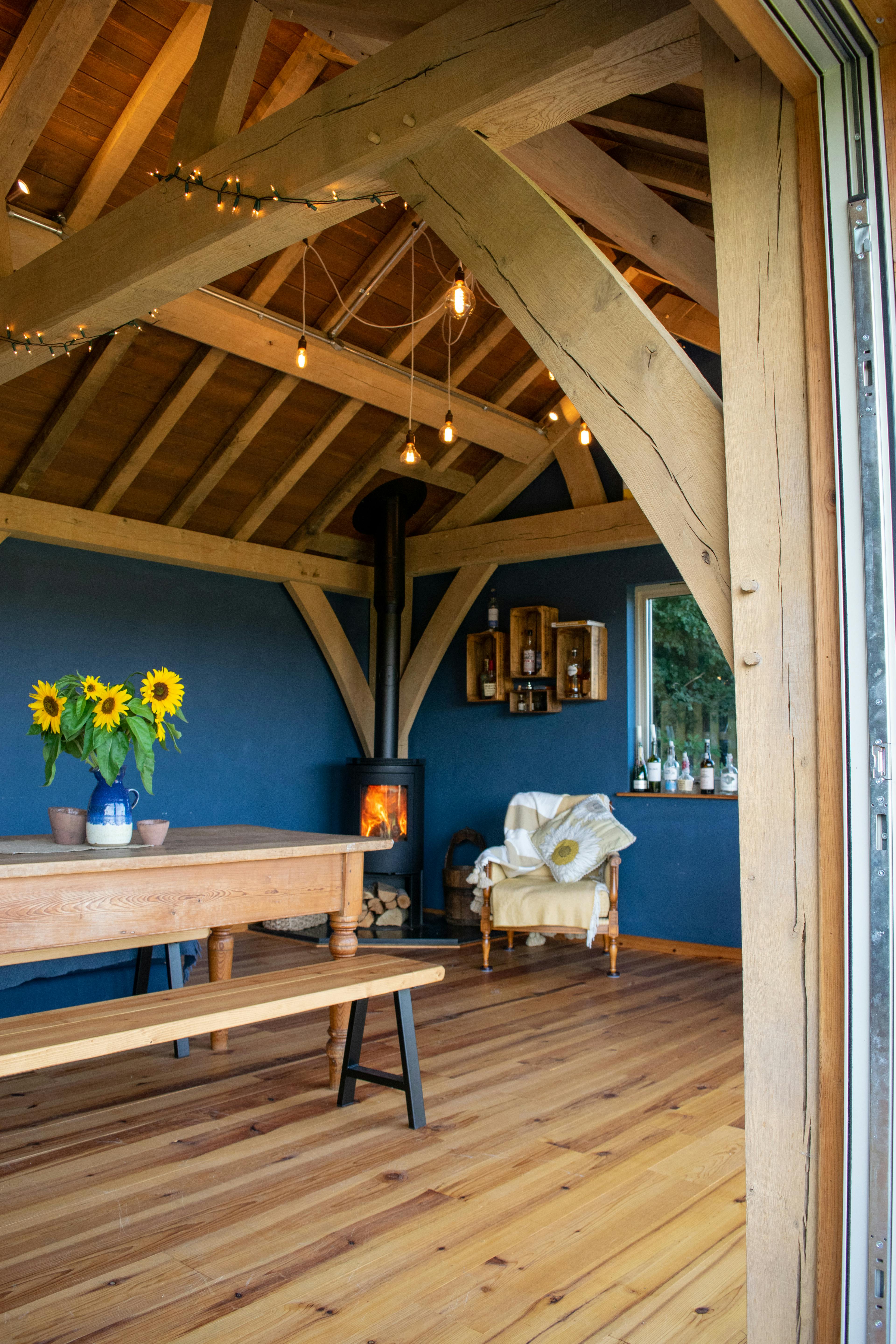 The inside of a 2-bay oak framed extension with a log burner and bi fold doors opening out to a garden