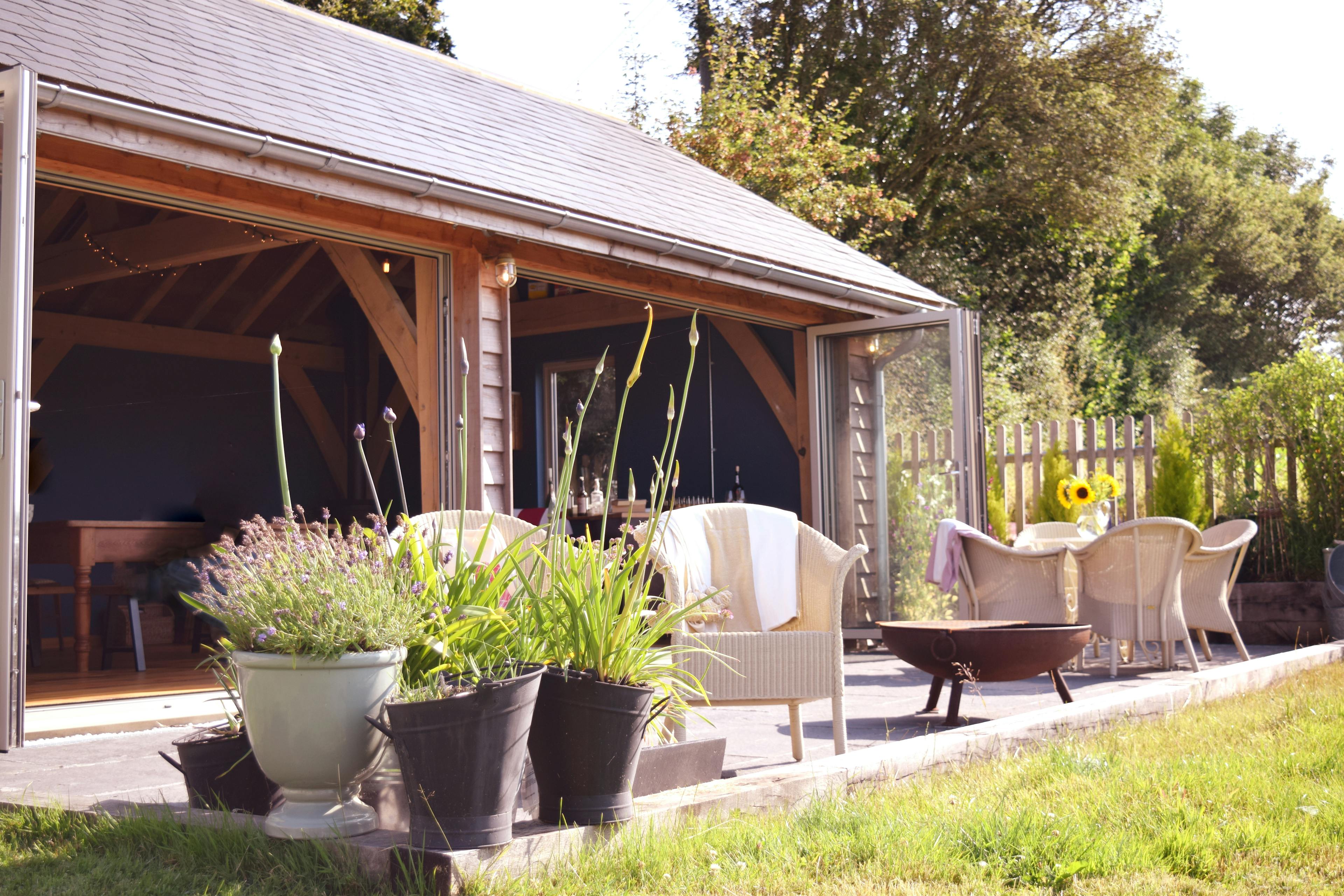 A 2-bay oak framed extension with bi-fold doors opening out to a garden with outdoor seating and a green lawn