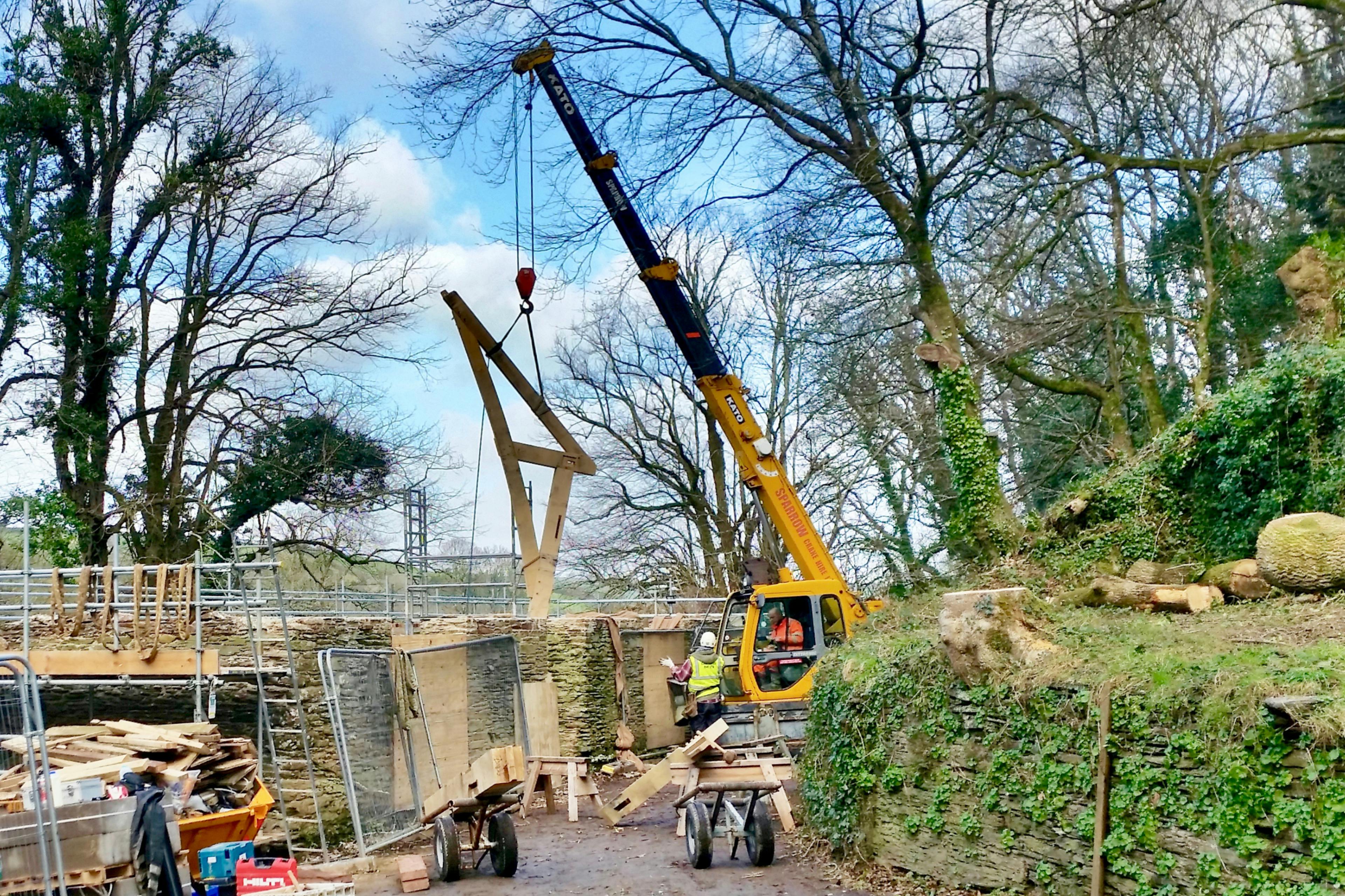 Image of a timber frame site installation, with a crane lifting a preassembled truss into place