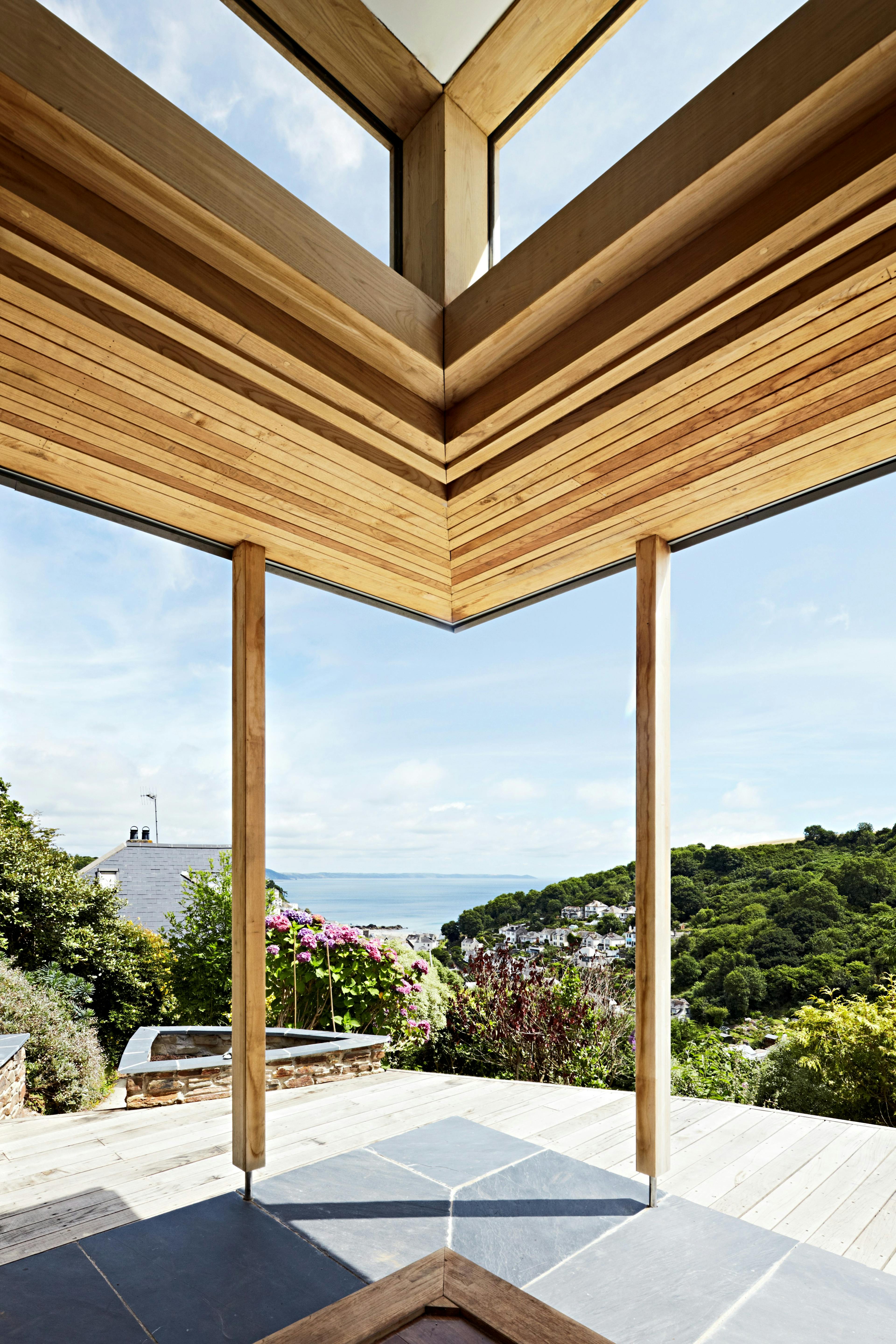 The corner of a chestnut glulam extension with wooden decking and views down to the sea