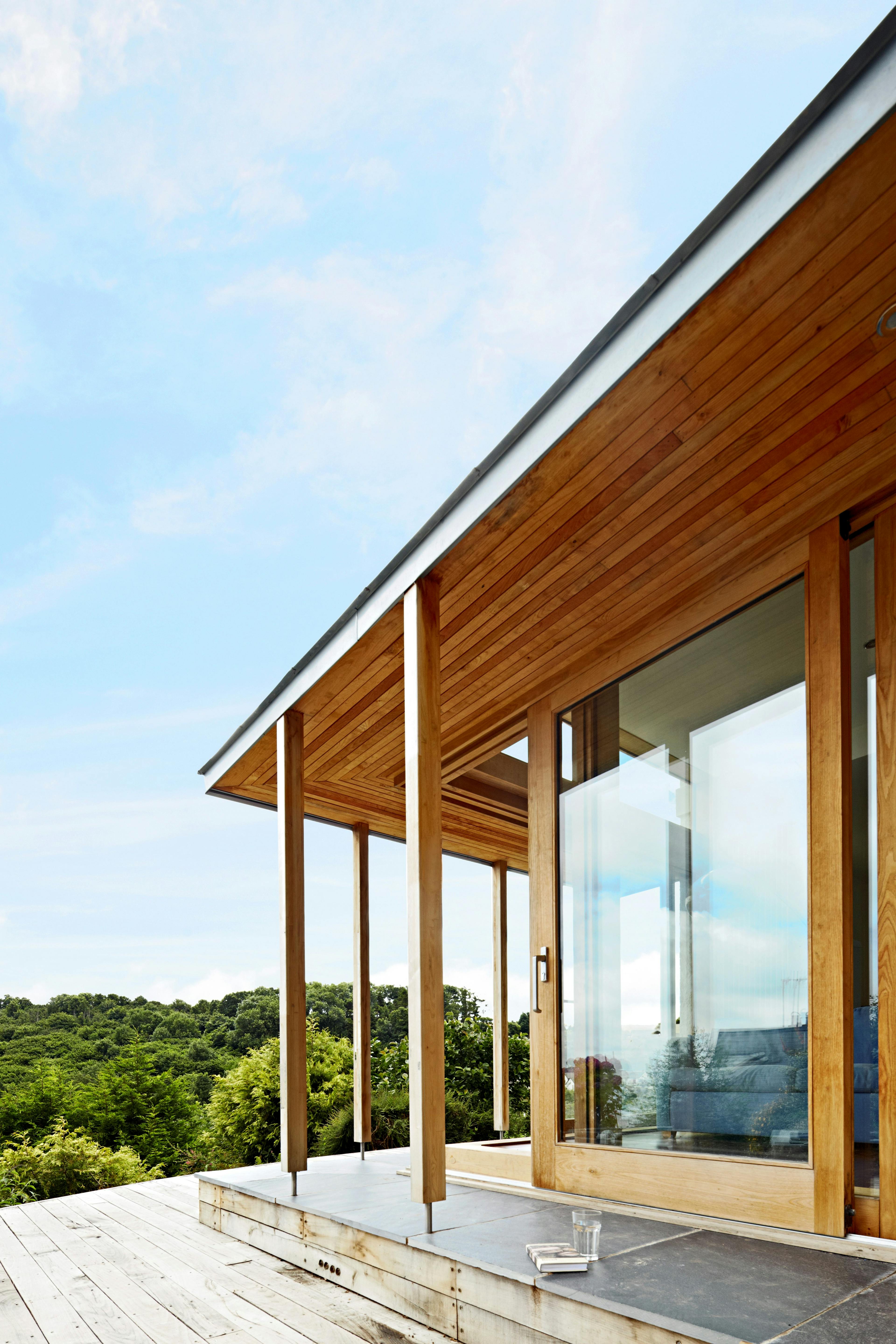 A chestnut glulam extension with wooden decking and views of the surrounding green countryside down to the sea