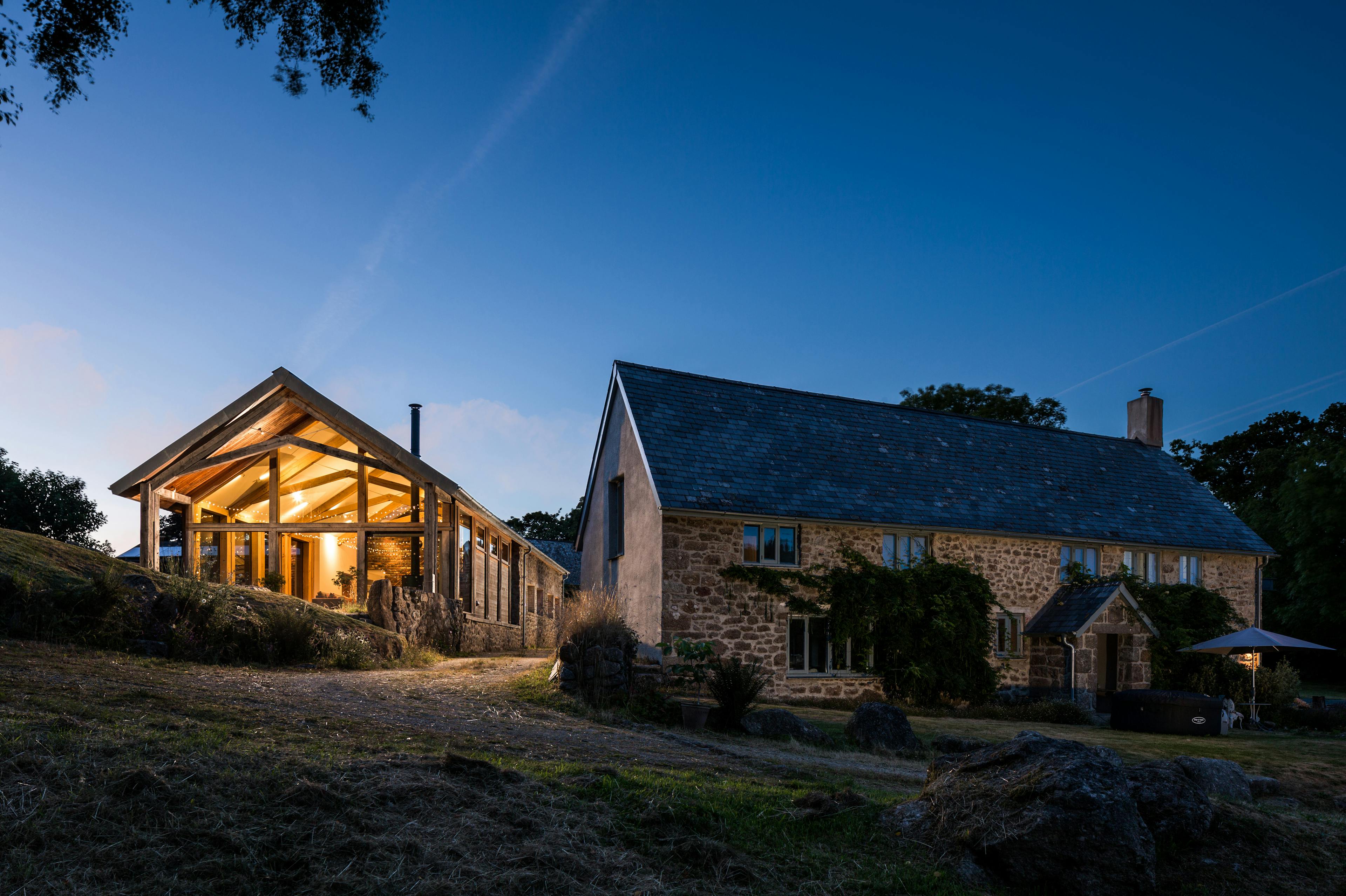 Exterior view of a self-contained annexe at night, featuring a glazed gable end with a structural oak frame