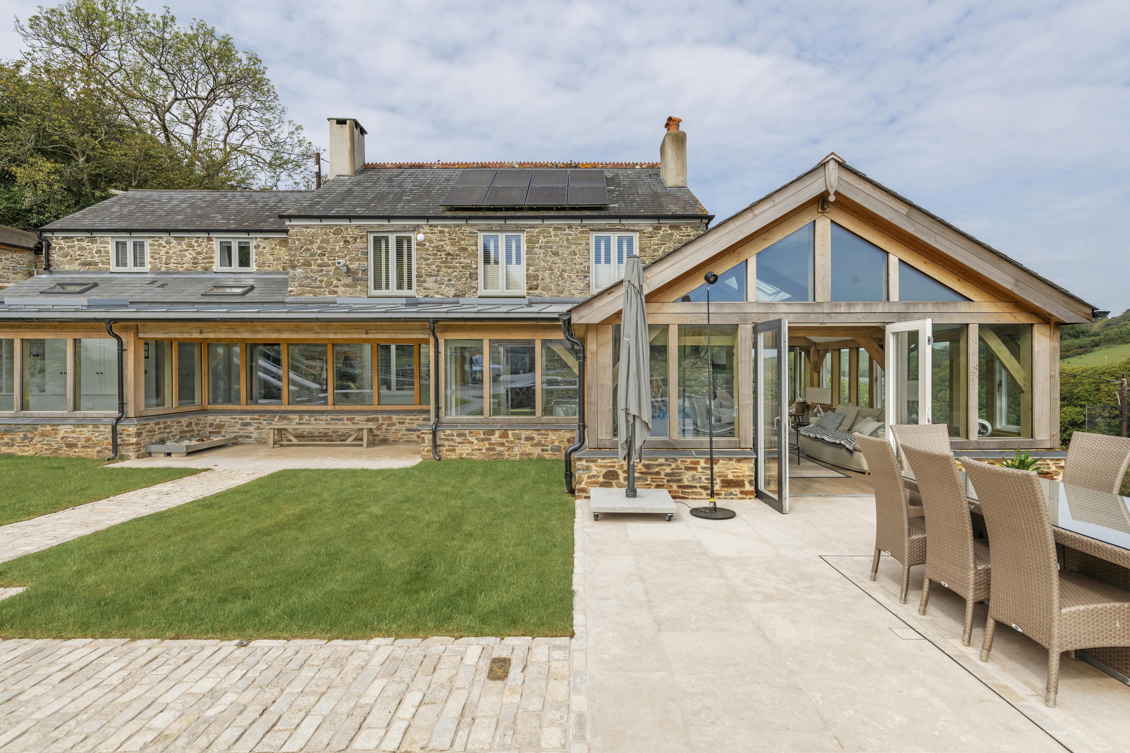 A renovated cottage on an estuary with a a green lawn, patio area, and oak framed garden room, entrance and corridor extension