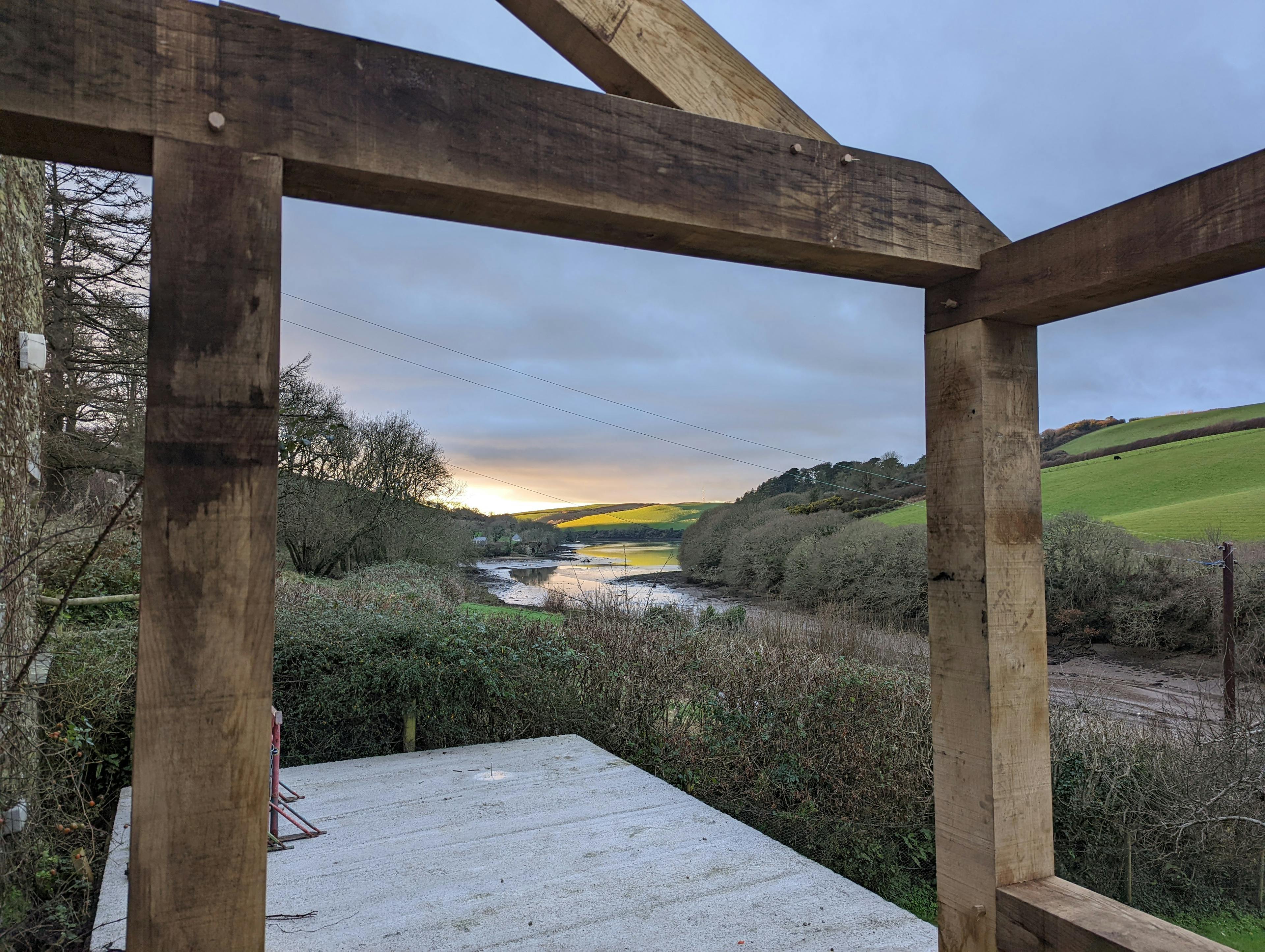 The frame for an oak framed garden room, entrance and corridor extension during installation with a sunset behind