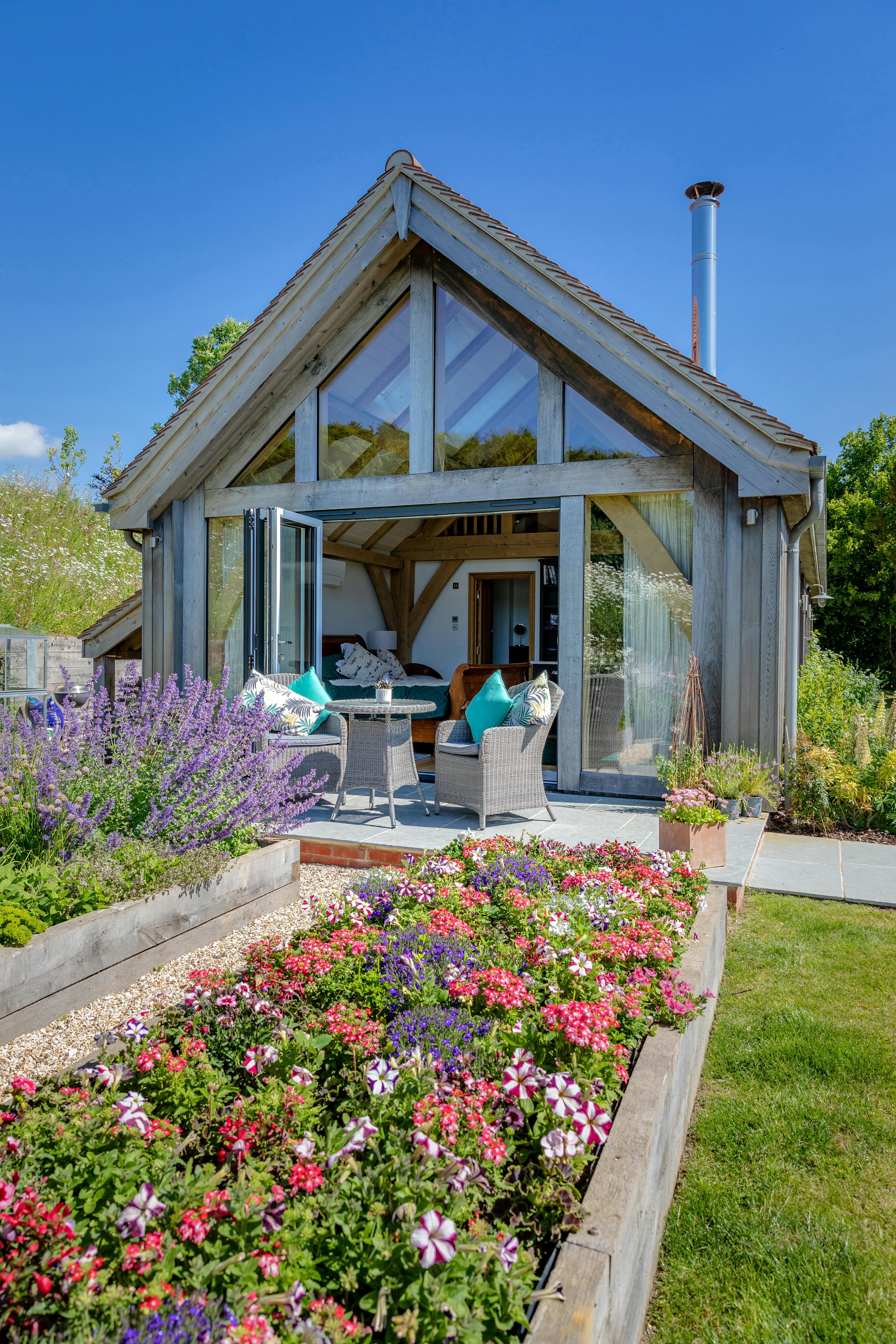 An oak framed garden annex with a glazed gable, with flower beds in front