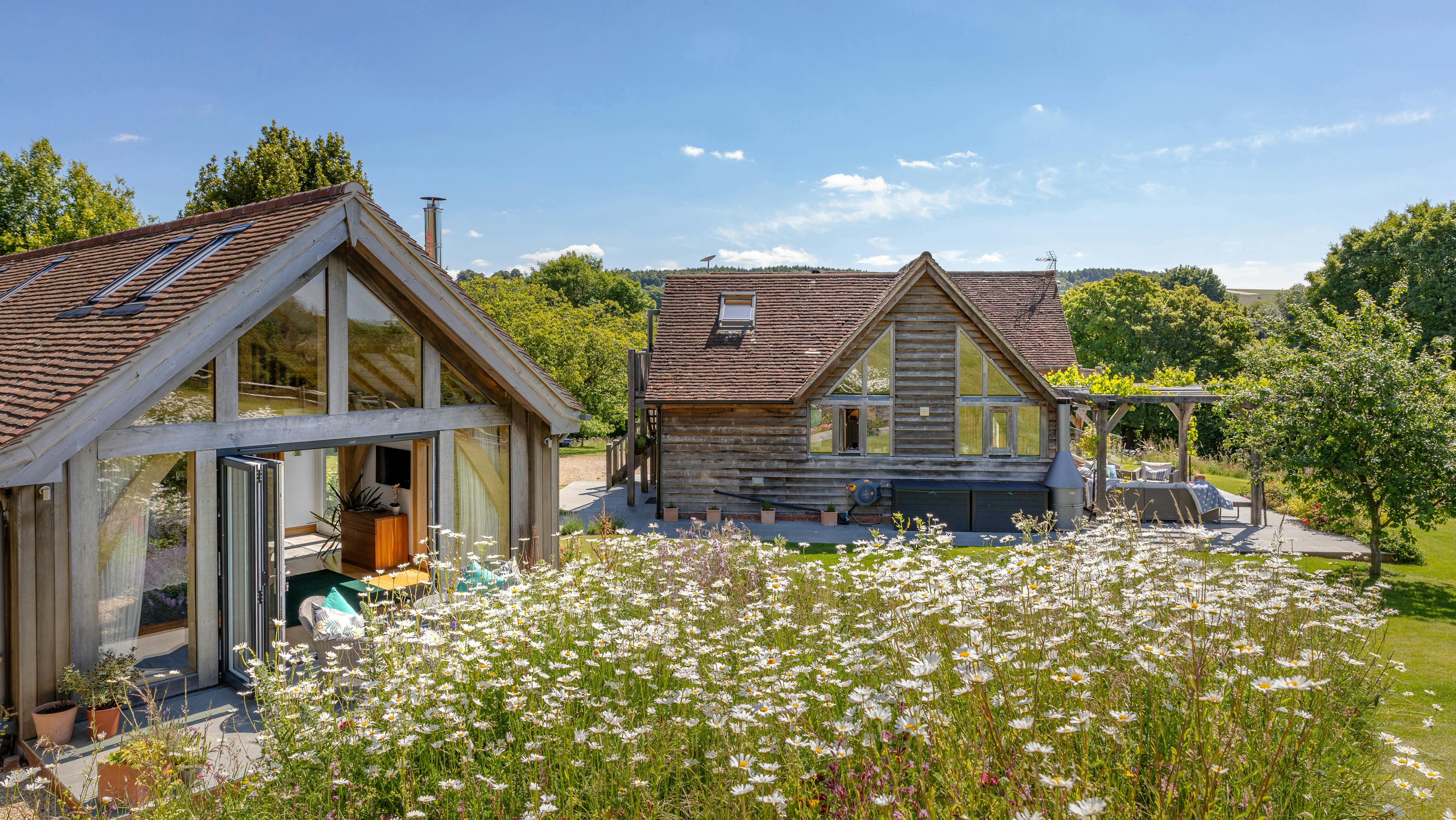 An oak framed garden annex with a glazed gable end and surrounded by a landscaped garden and an oak framed home close by