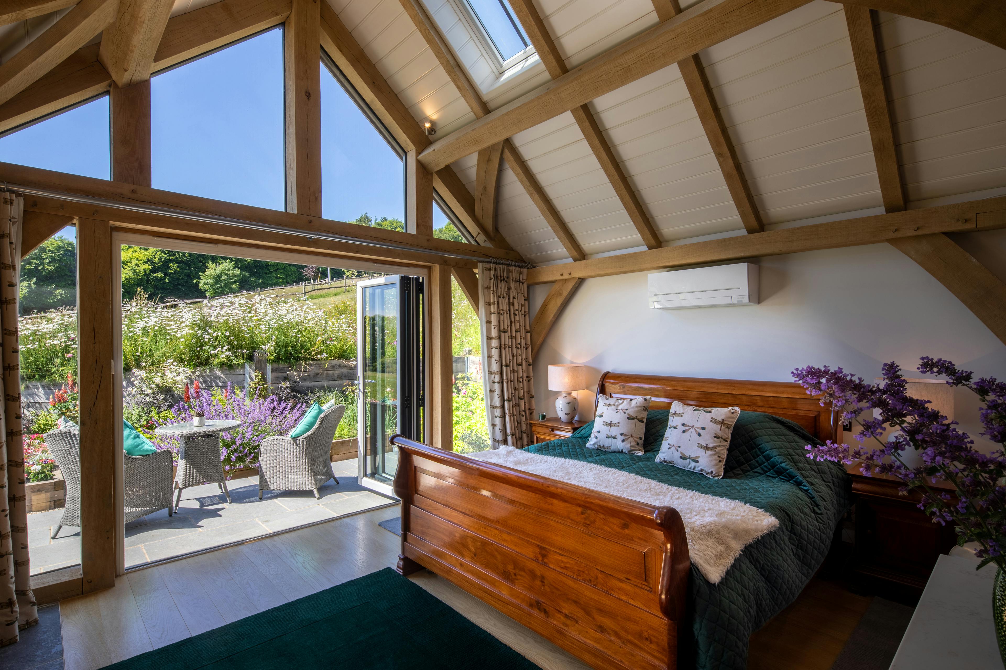 The bedroom area inside an oak framed garden annex with a glazed gable end and doors opening to a patio