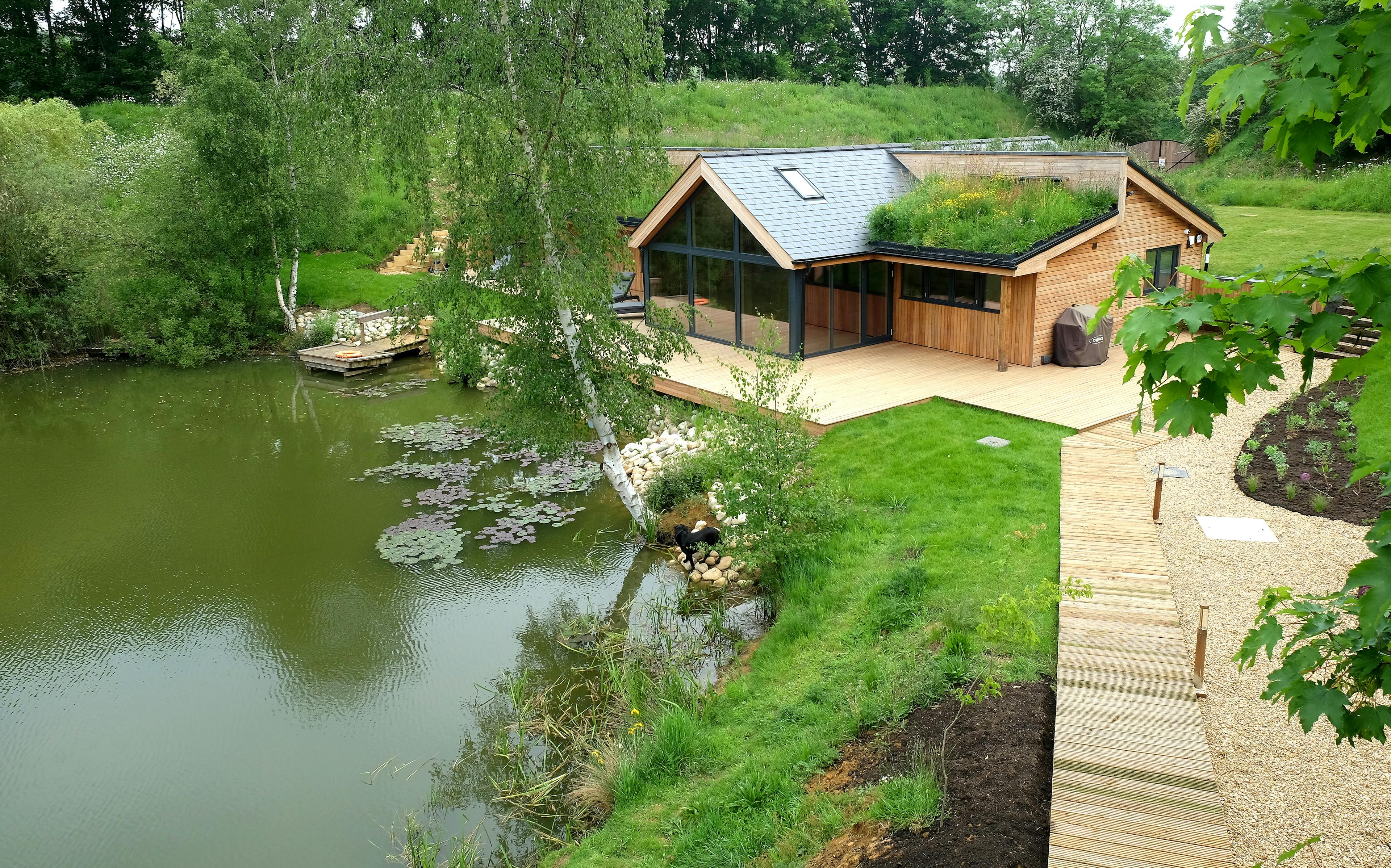 Aerial view of an oak-framed bungalow located on the shore of a lake, with a timber walkway leading to it