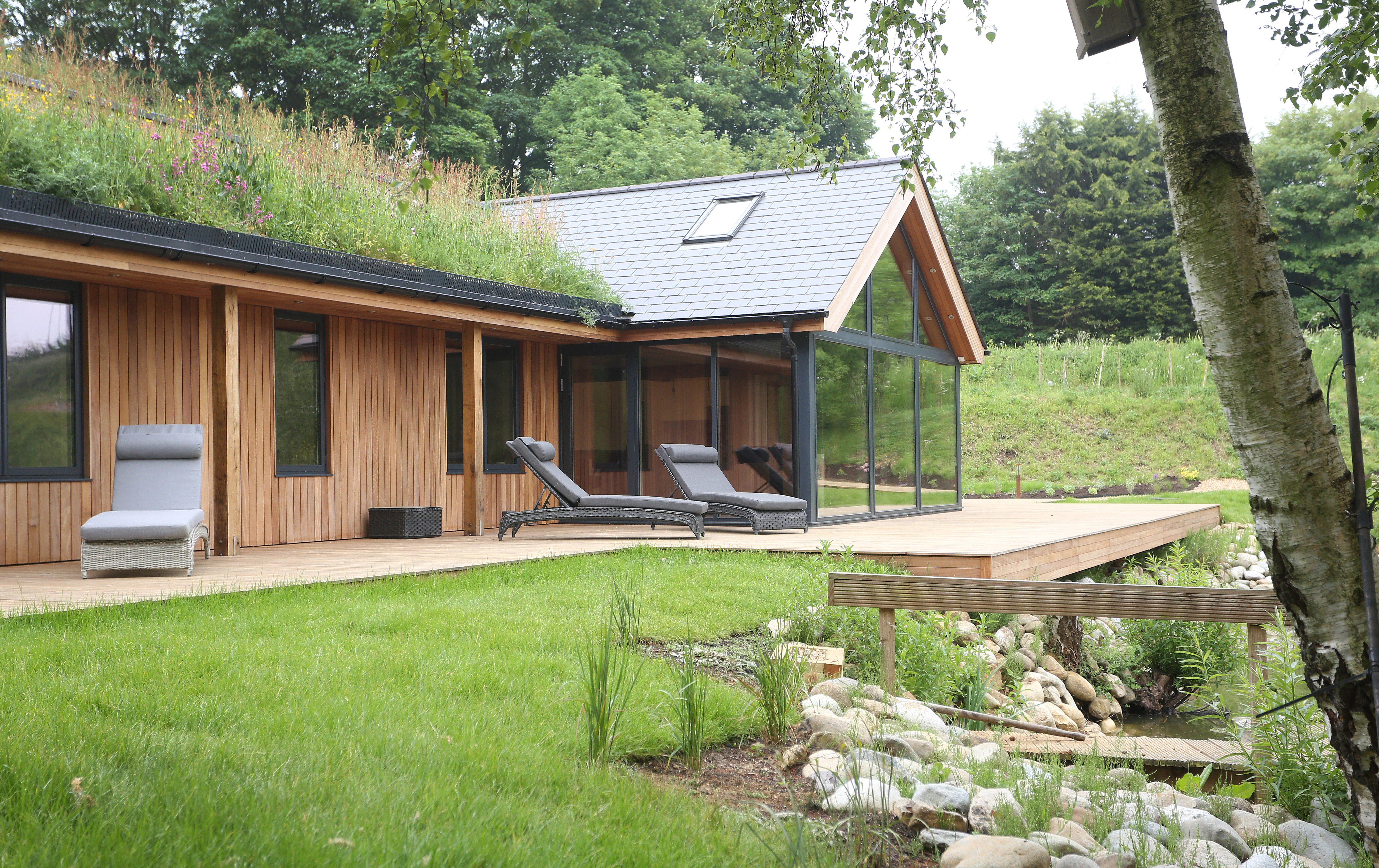 Oak-framed bungalow with a green living roof, situated on the shore of a lake, featuring modern decking