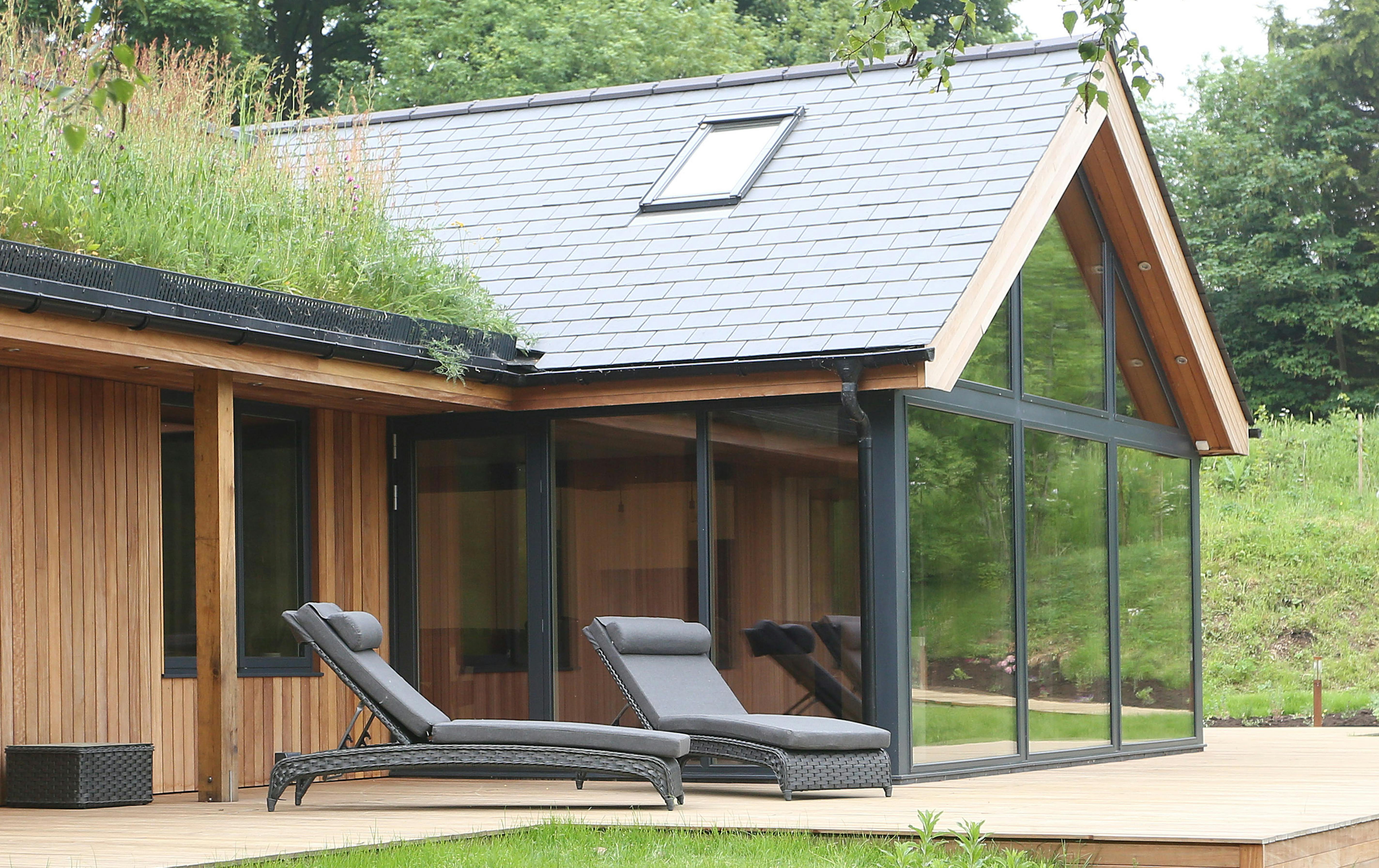Oak-framed bungalow with a green living roof, situated on the shore of a lake, featuring modern decking