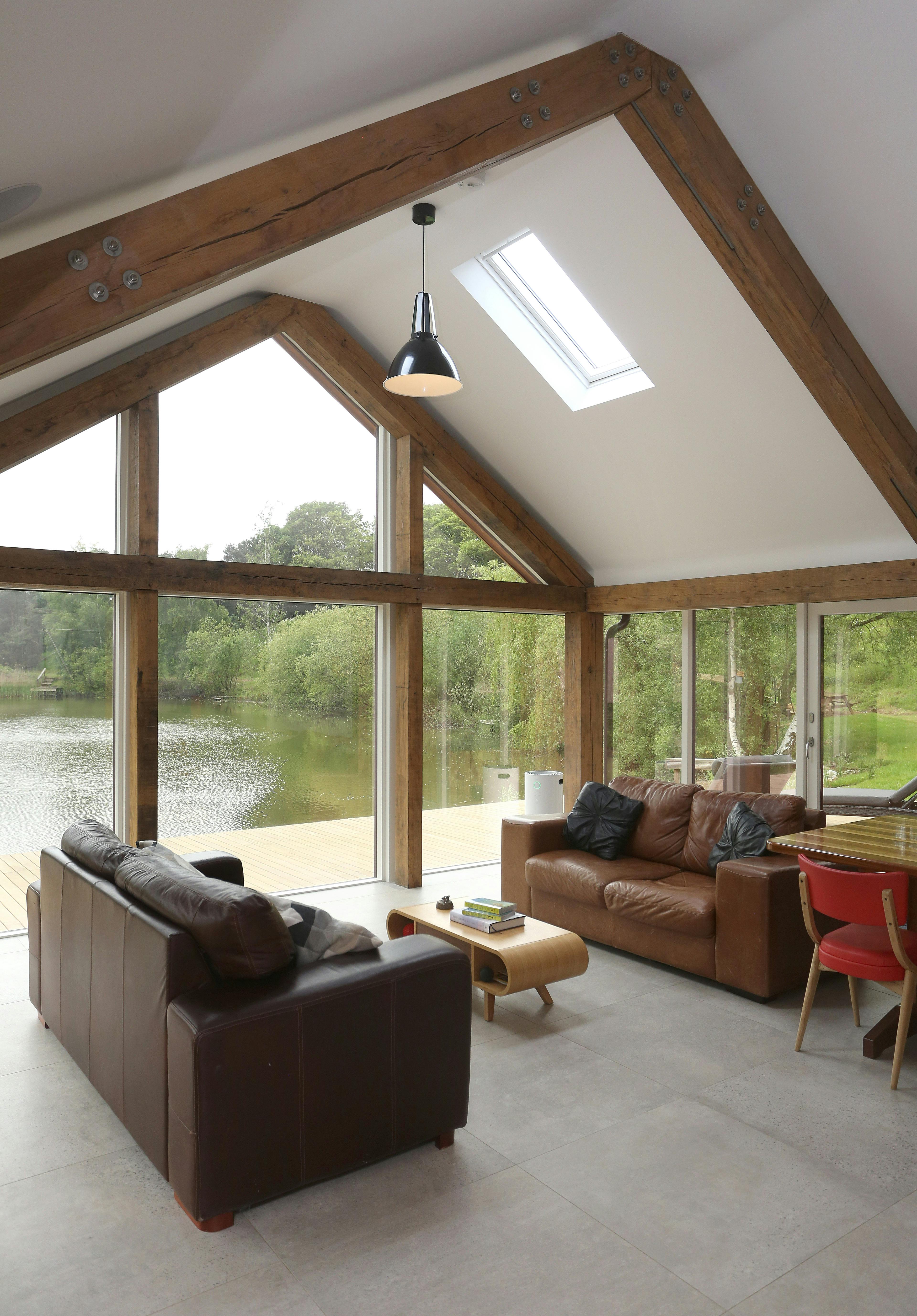 Interior view of an open-plan living area with a full-height glazed gable end, offering views of picturesque lakes