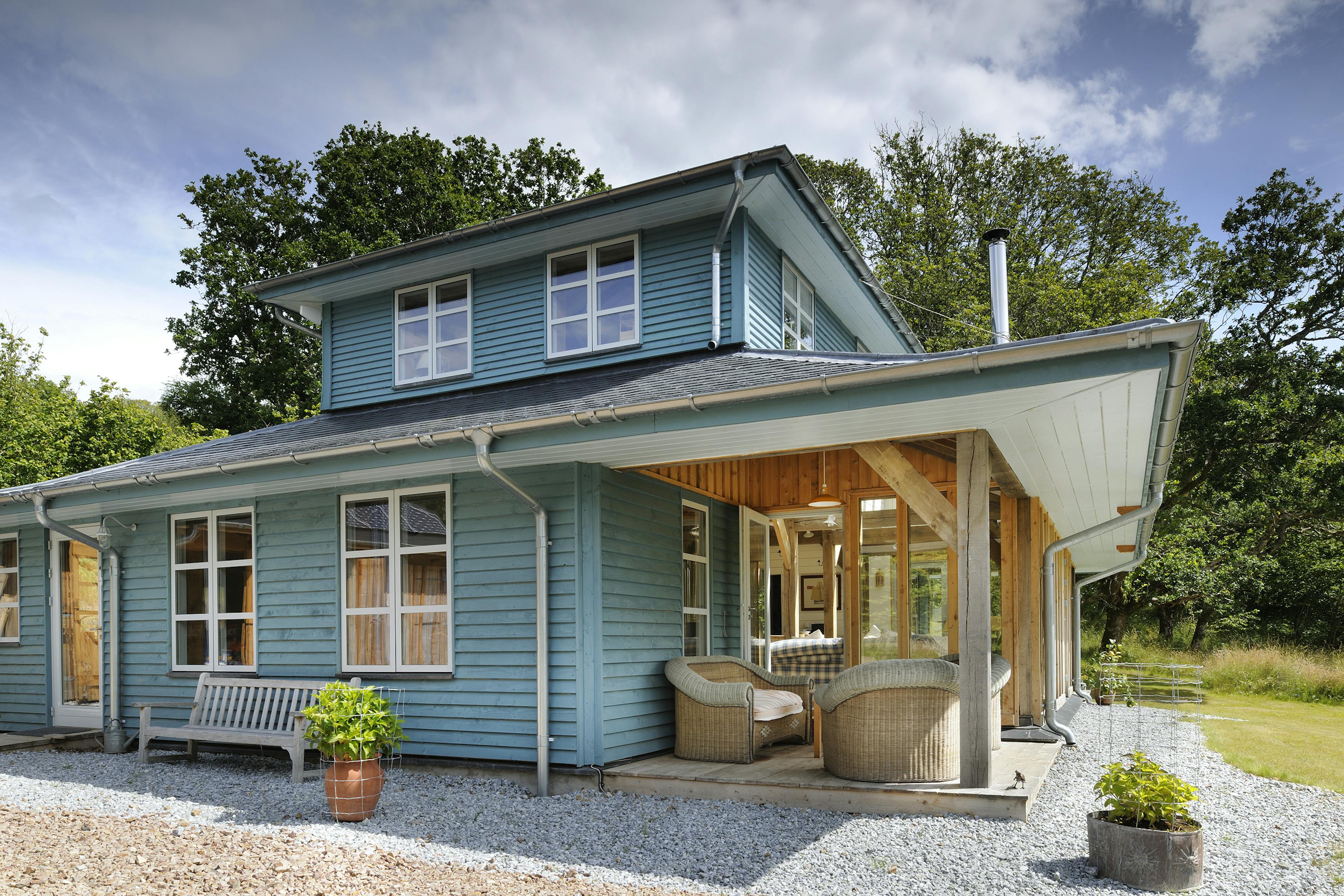 Exterior view of a two-storey oak-framed guest house with a wrap-around veranda, set along the coast