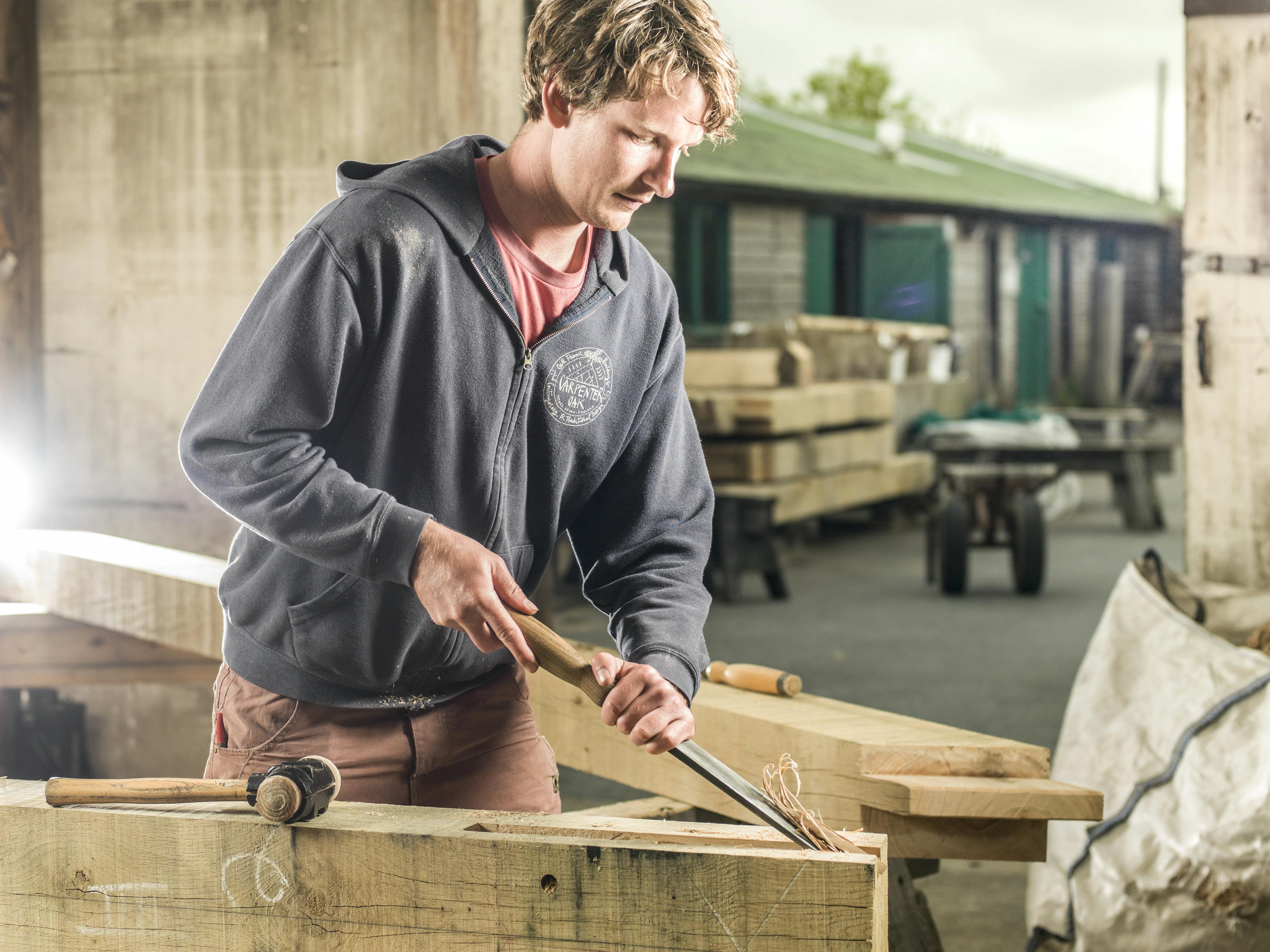 A carpenter uses a tool to hand craft a timber frame