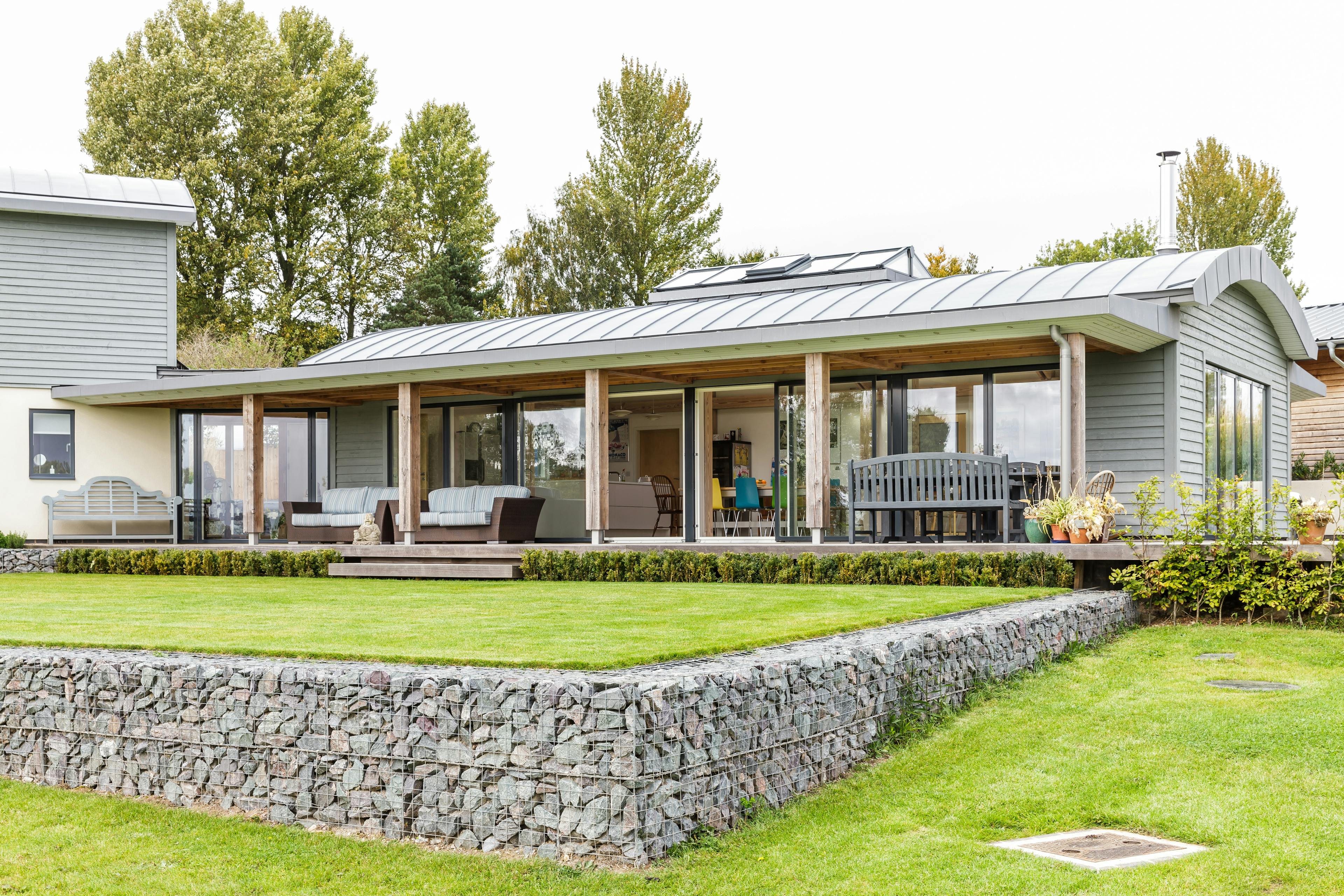 Exterior view of a contemporary family home with a pergola-style structure providing coverage over the wraparound decking