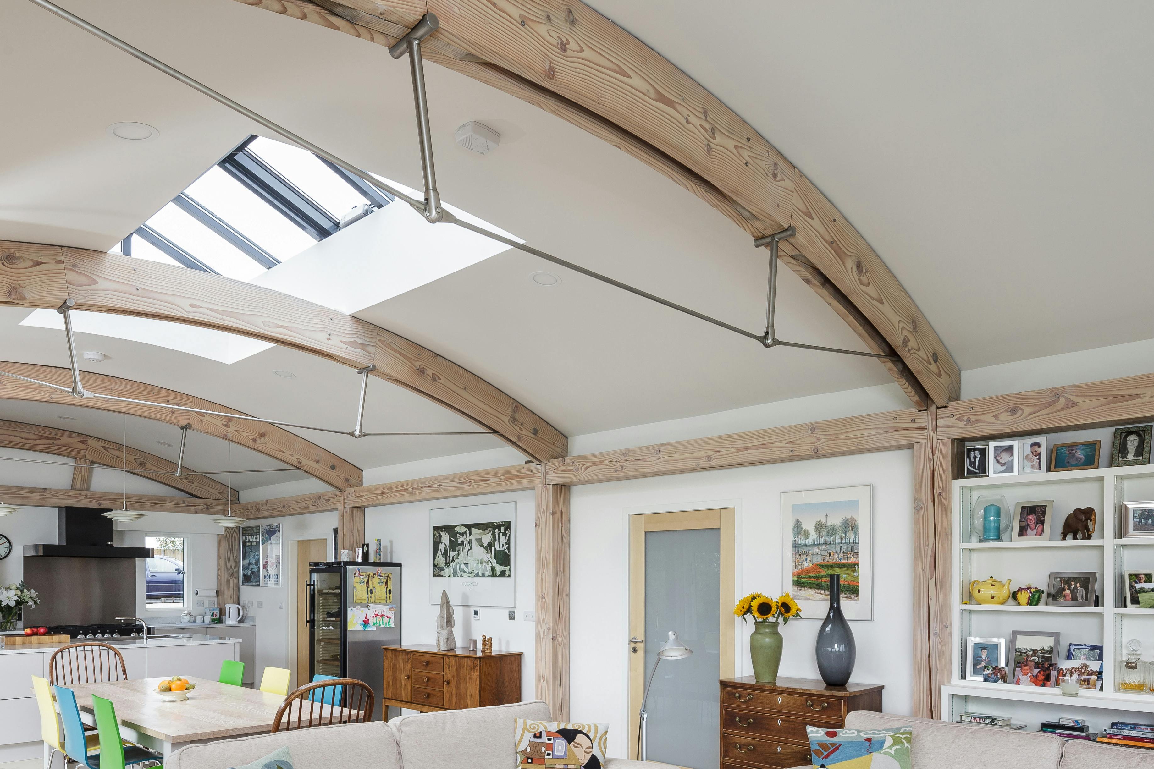 Interior view of an open-plan living space with exposed curved Douglas fir beams and steel connections