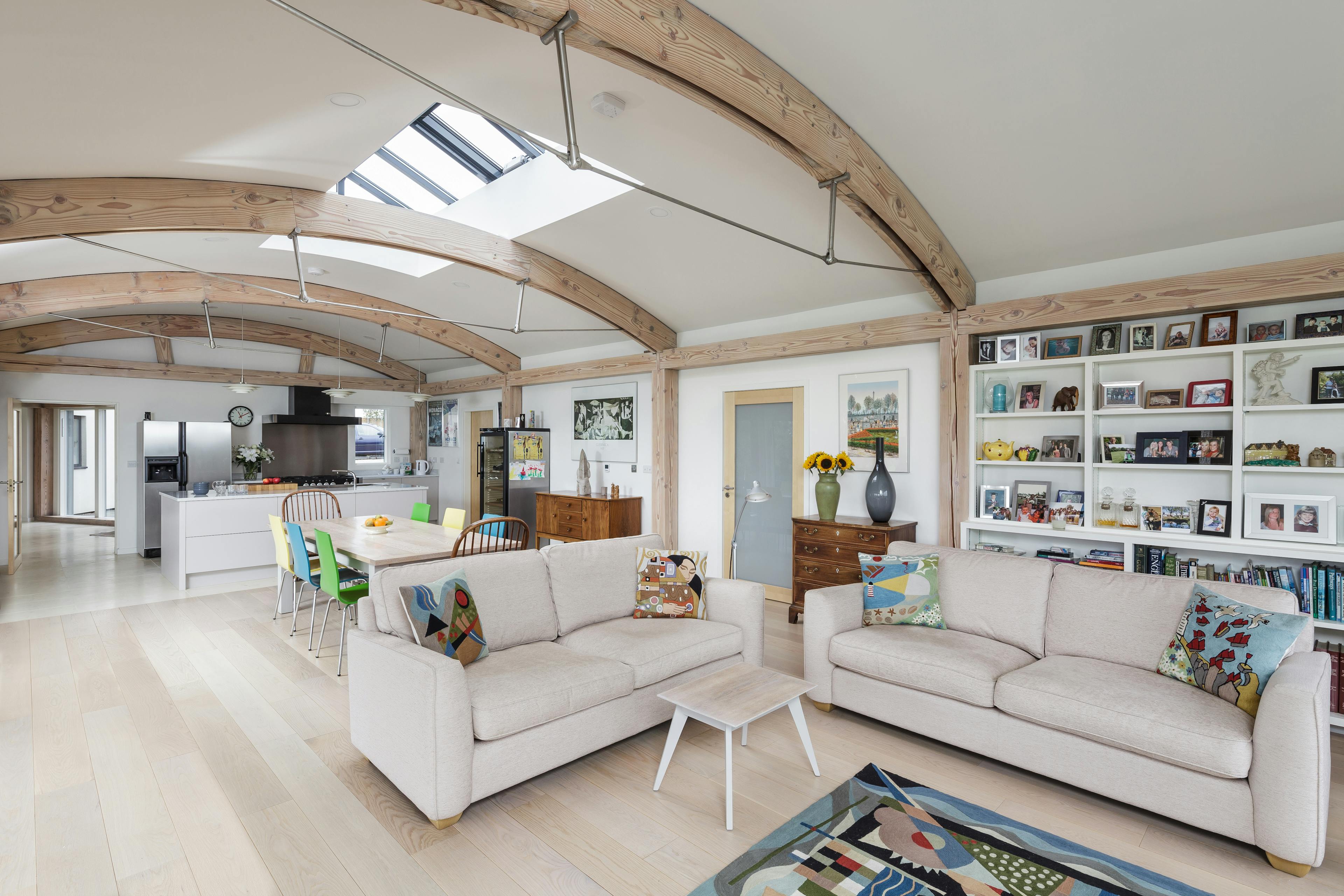 Interior view of an open-plan living space with exposed curved Douglas fir beams and steel connections