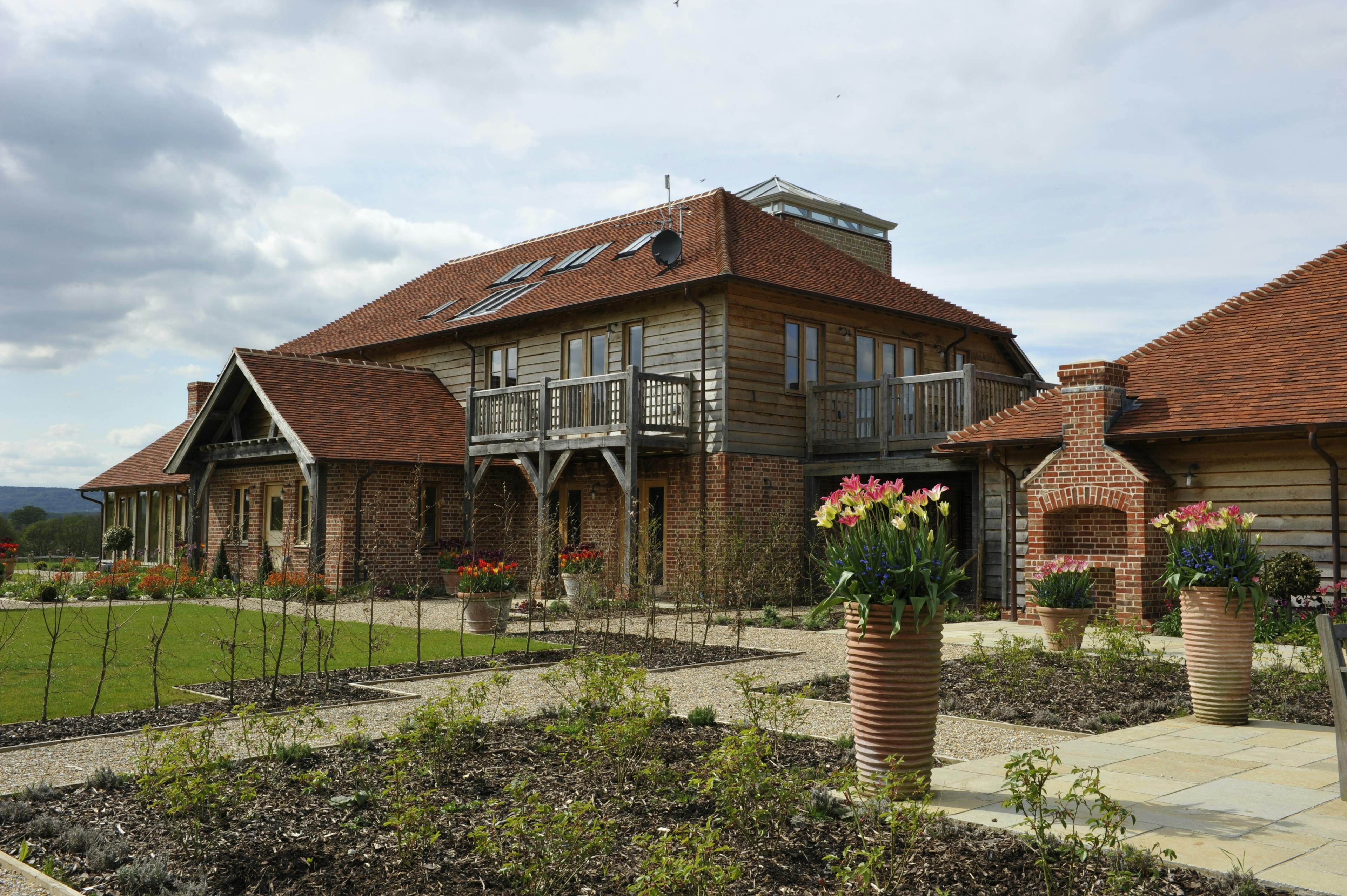 Exterior view of a farmhouse-style country home with wraparound balconies, a landscaped garden