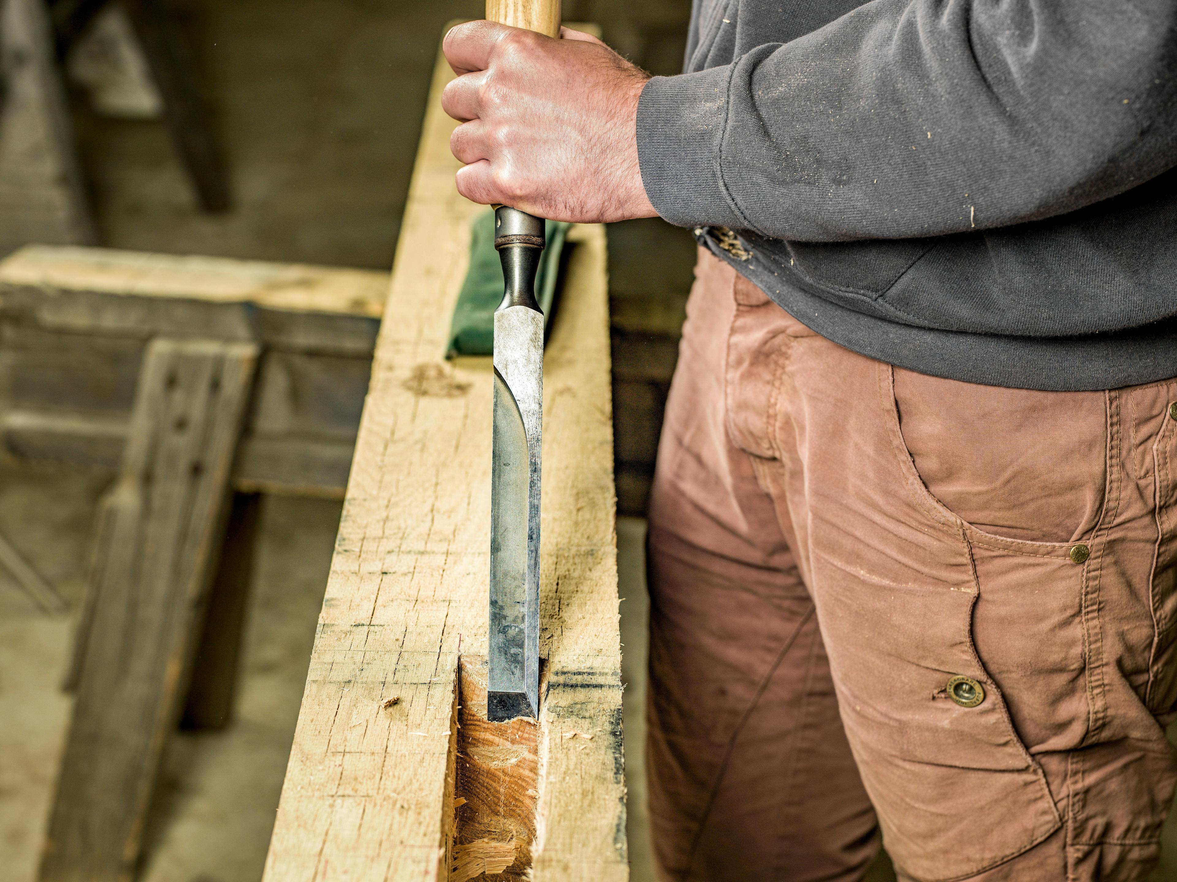 A carpenter in a workshop chisels into an oak frame for a structural timber frame