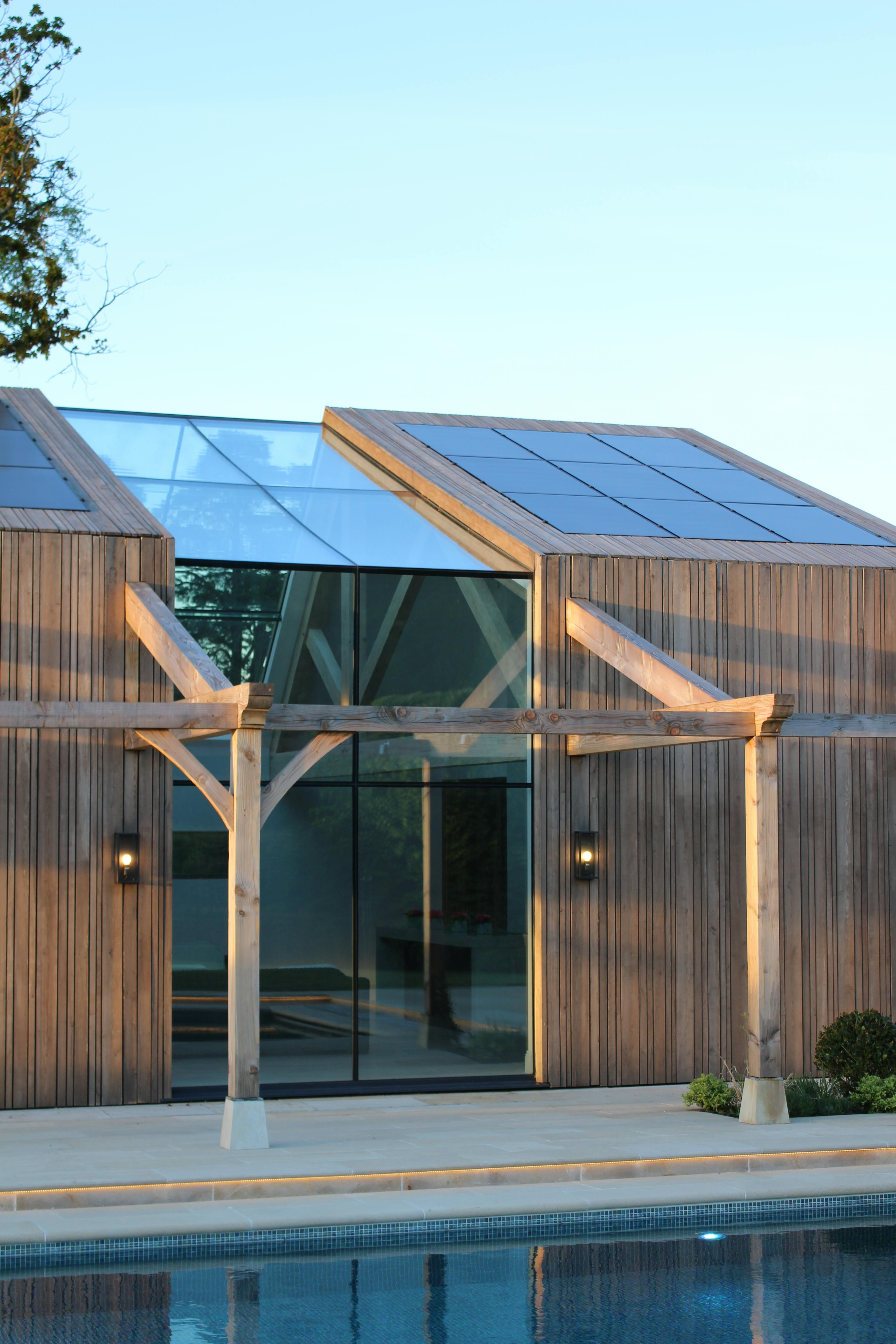 Exterior view of a contemporary glulam-framed pool house featuring full-height glazed panels