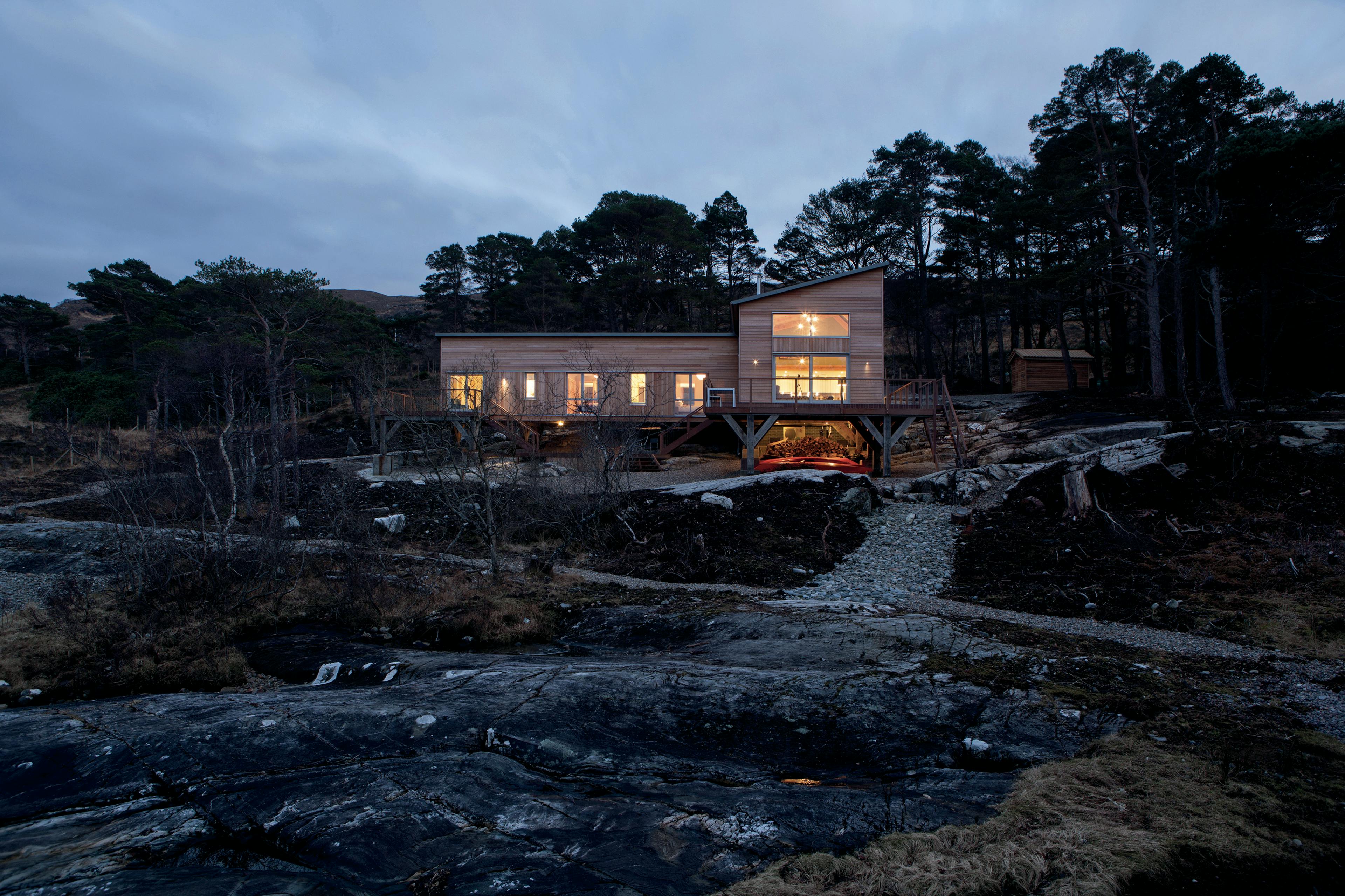 Exterior view of a Douglas fir-framed home built on a sloping, rocky shoreline of a loch