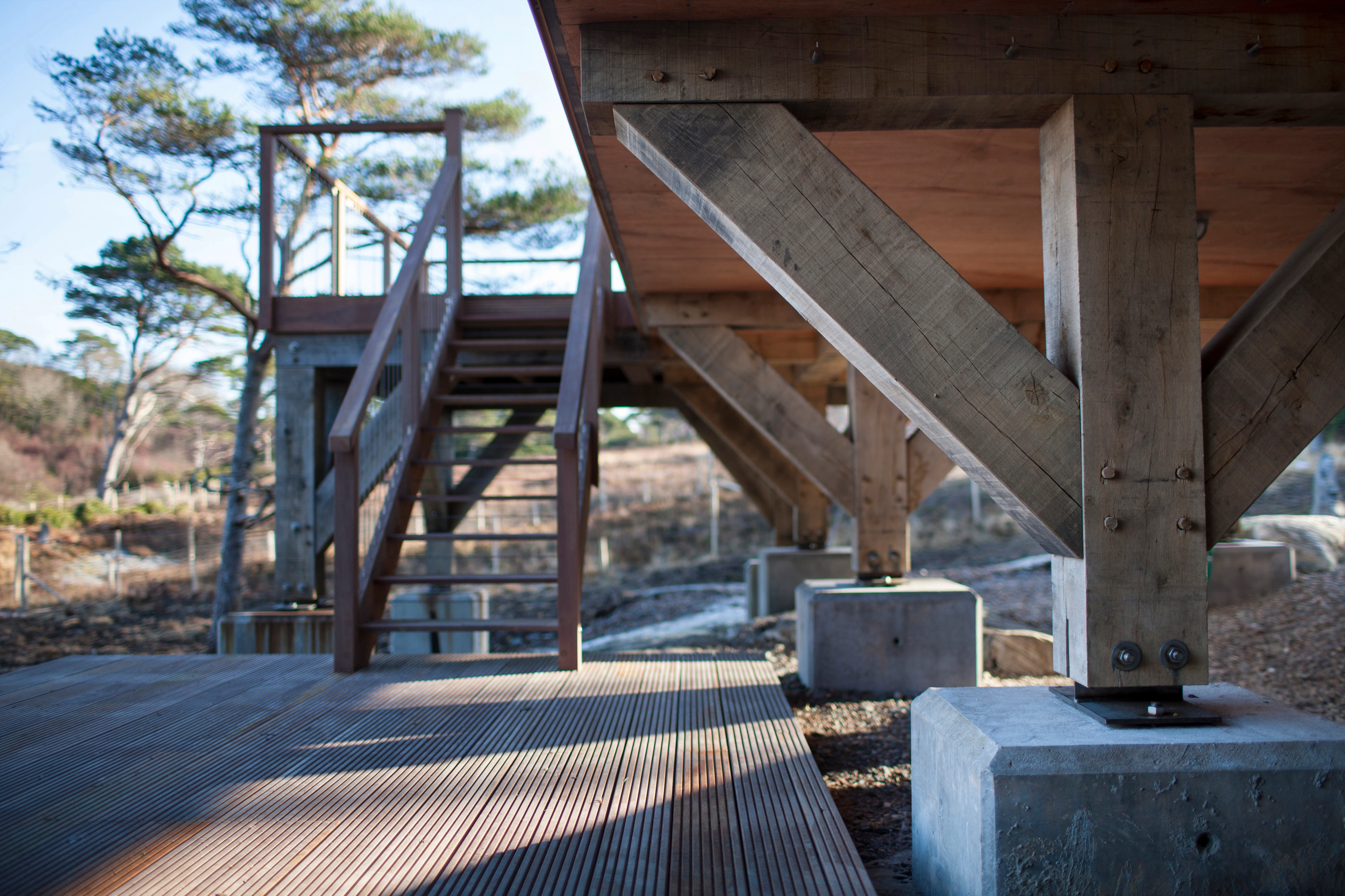 Close-up of concrete plinths with timber posts secured by steel connections on a sloping site