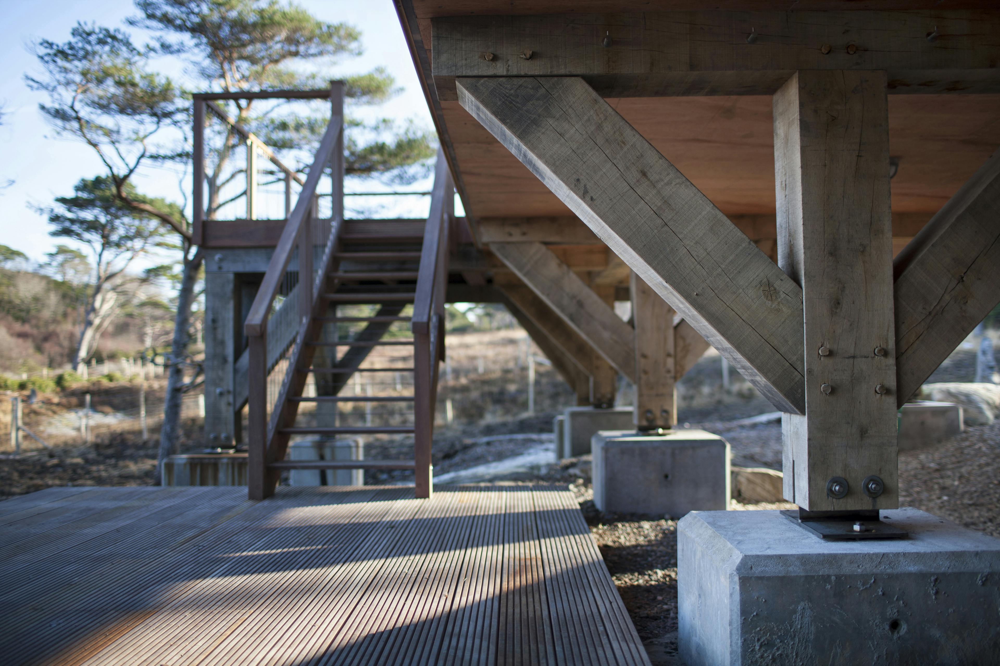 Close-up of concrete plinths with timber posts secured by steel connections on a sloping site