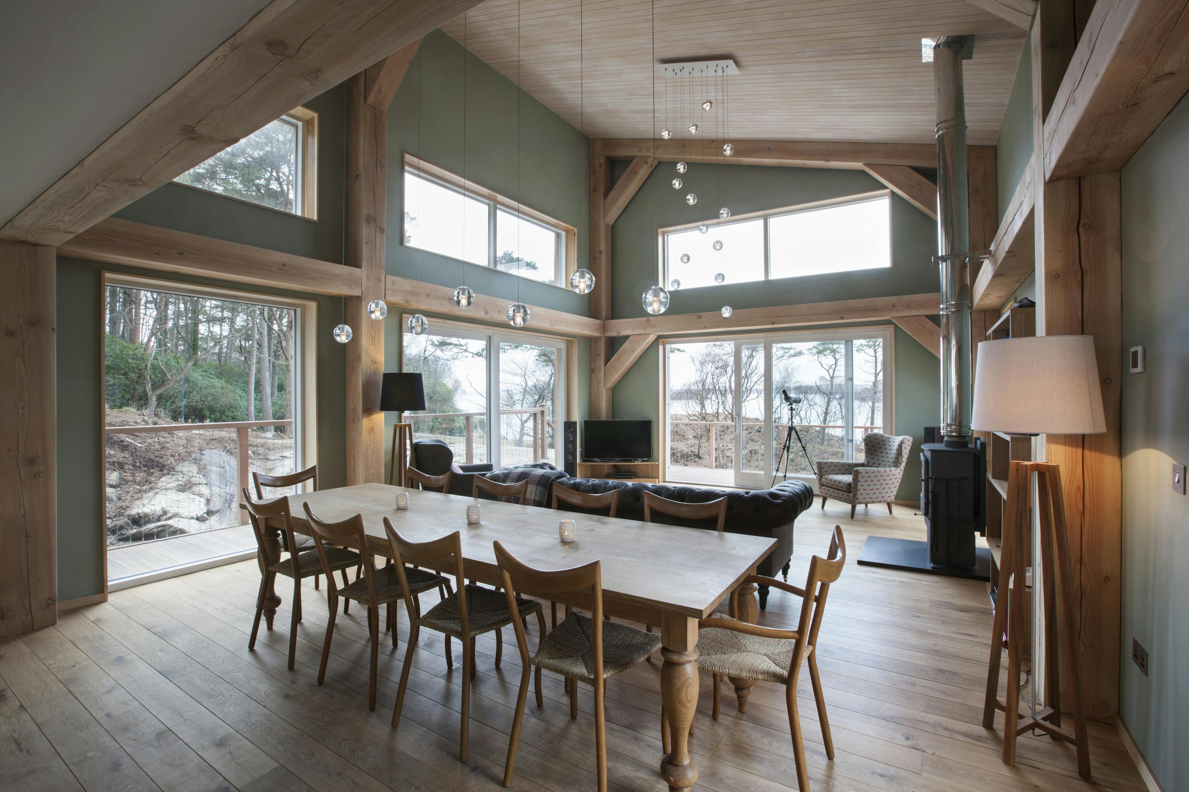 A dining table and sitting area with a log burner in a Douglas fir framed living room with a mono pitch