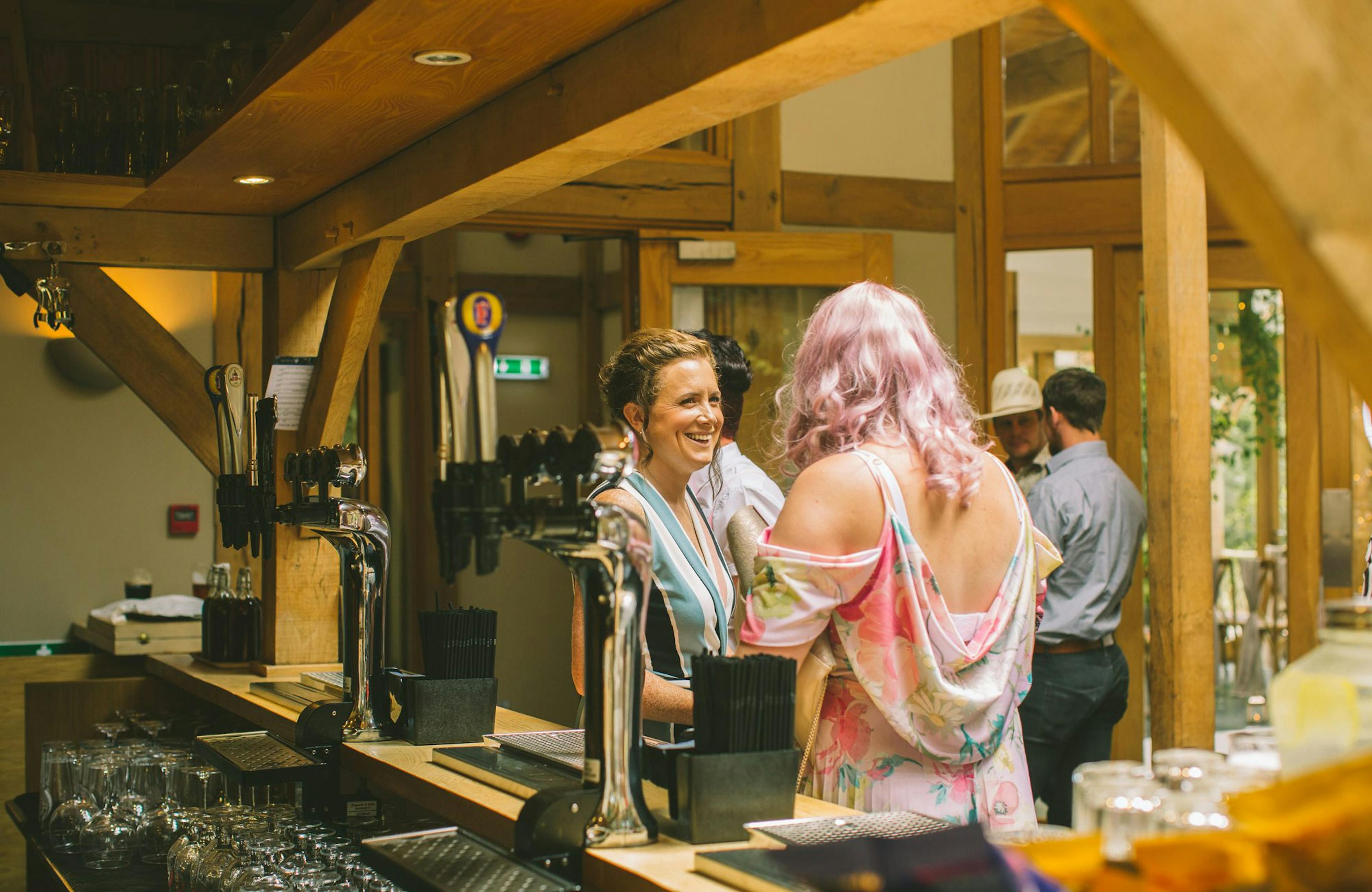 Wedding guests at the bar inside a rustic, oak-framed wedding barn