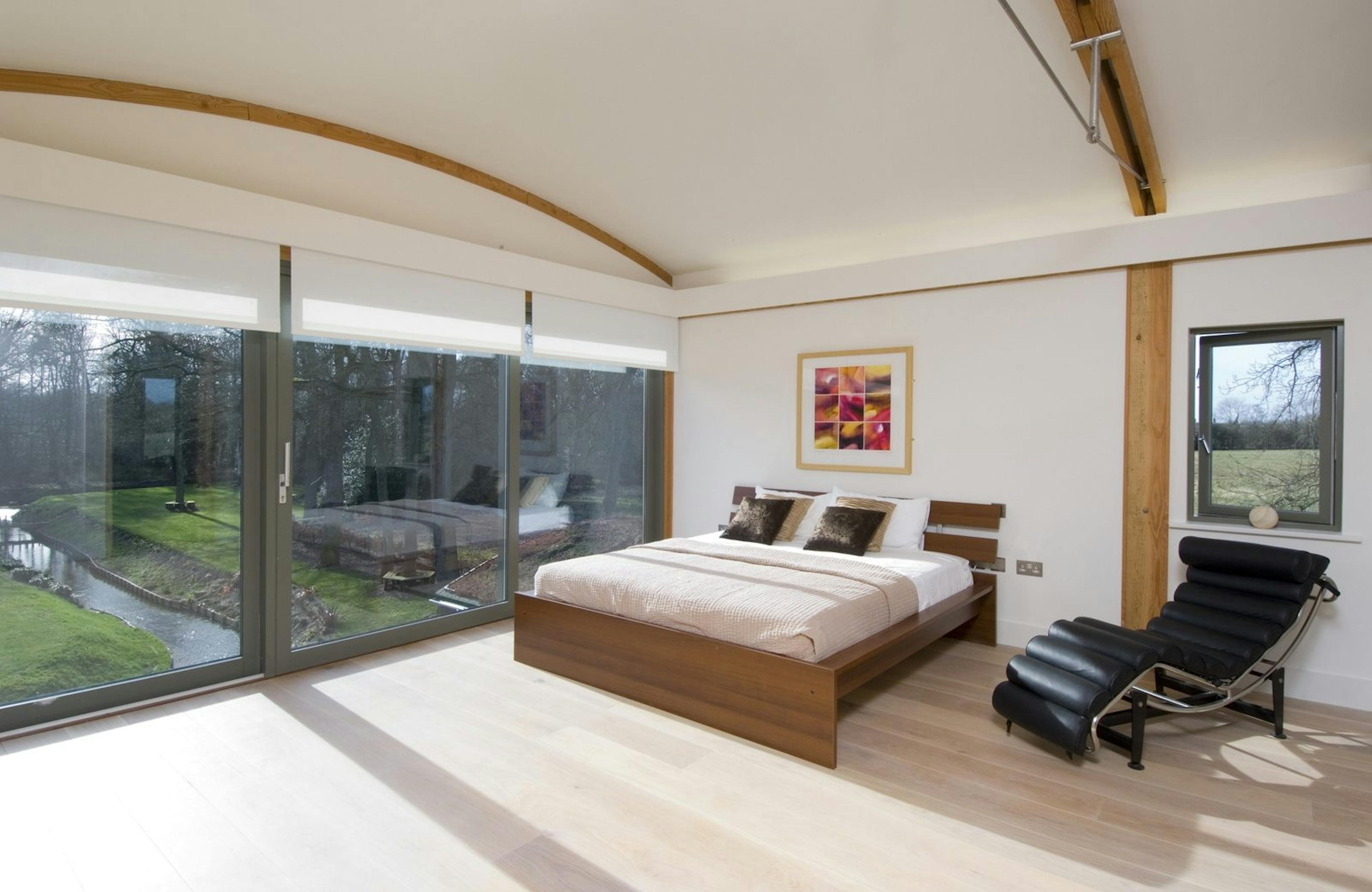 Bedroom with Expansive Glazing Offering Panoramic Garden Views, Highlighting Douglas Fir-Framed Curved Trusses and Modern Features