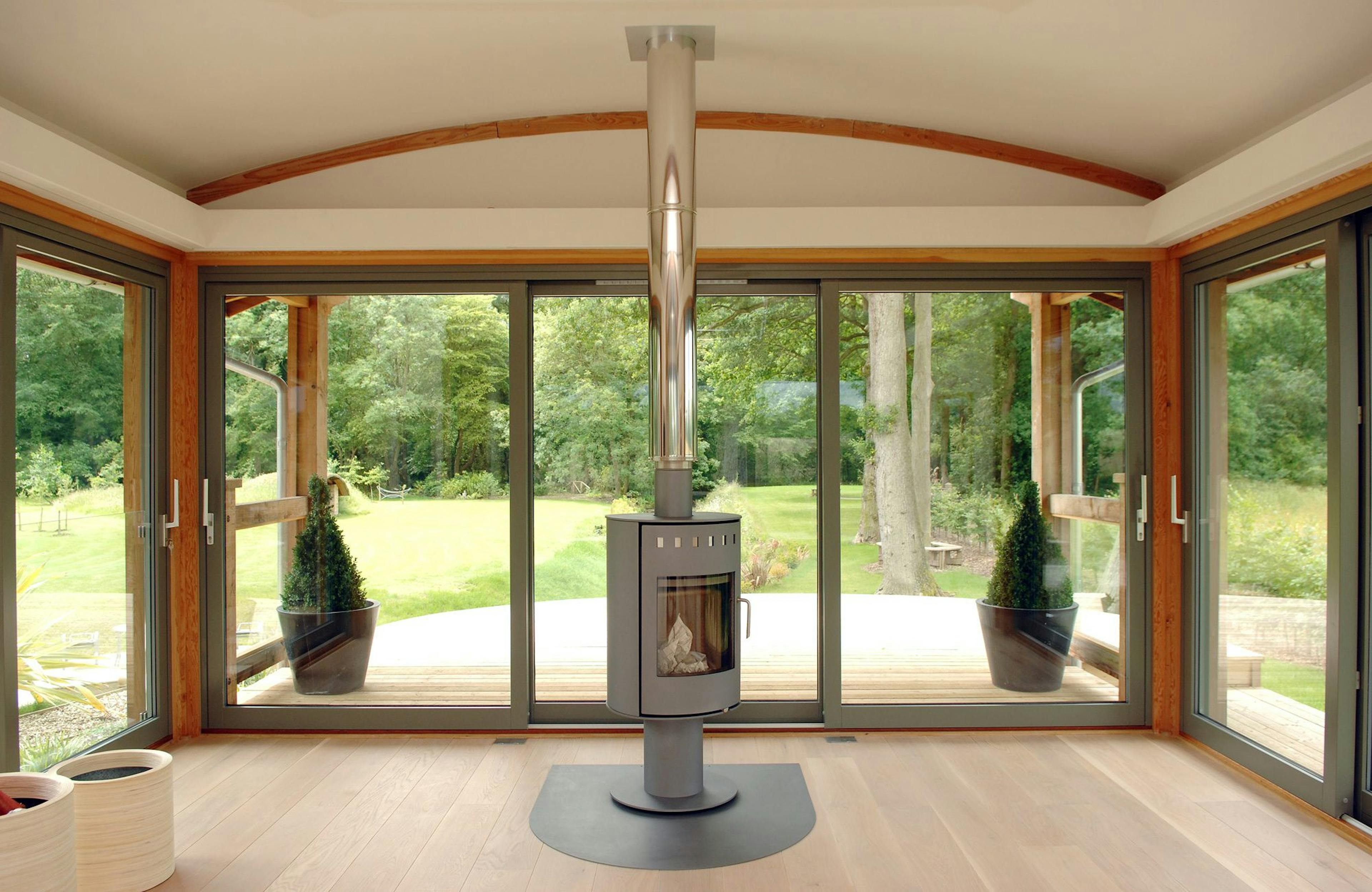 Douglas Fir-Framed Lounge Featuring a Central Log Burner, Curved Trusses with Steel Fixings for a Contemporary Touch, and Wrap-Around Glazing