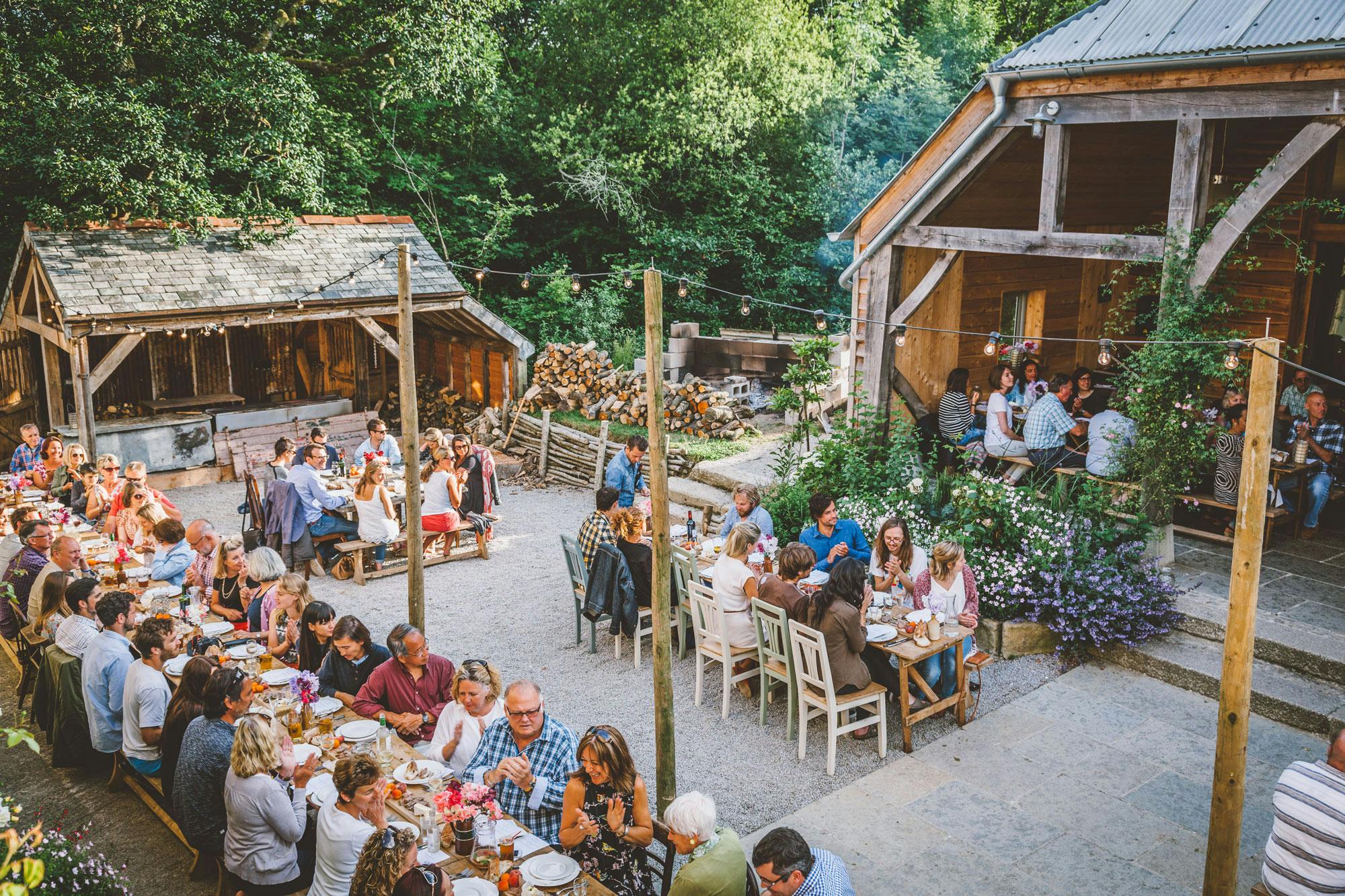 Guests seated on tables enjoying a meal outside an oak framed wedding barn