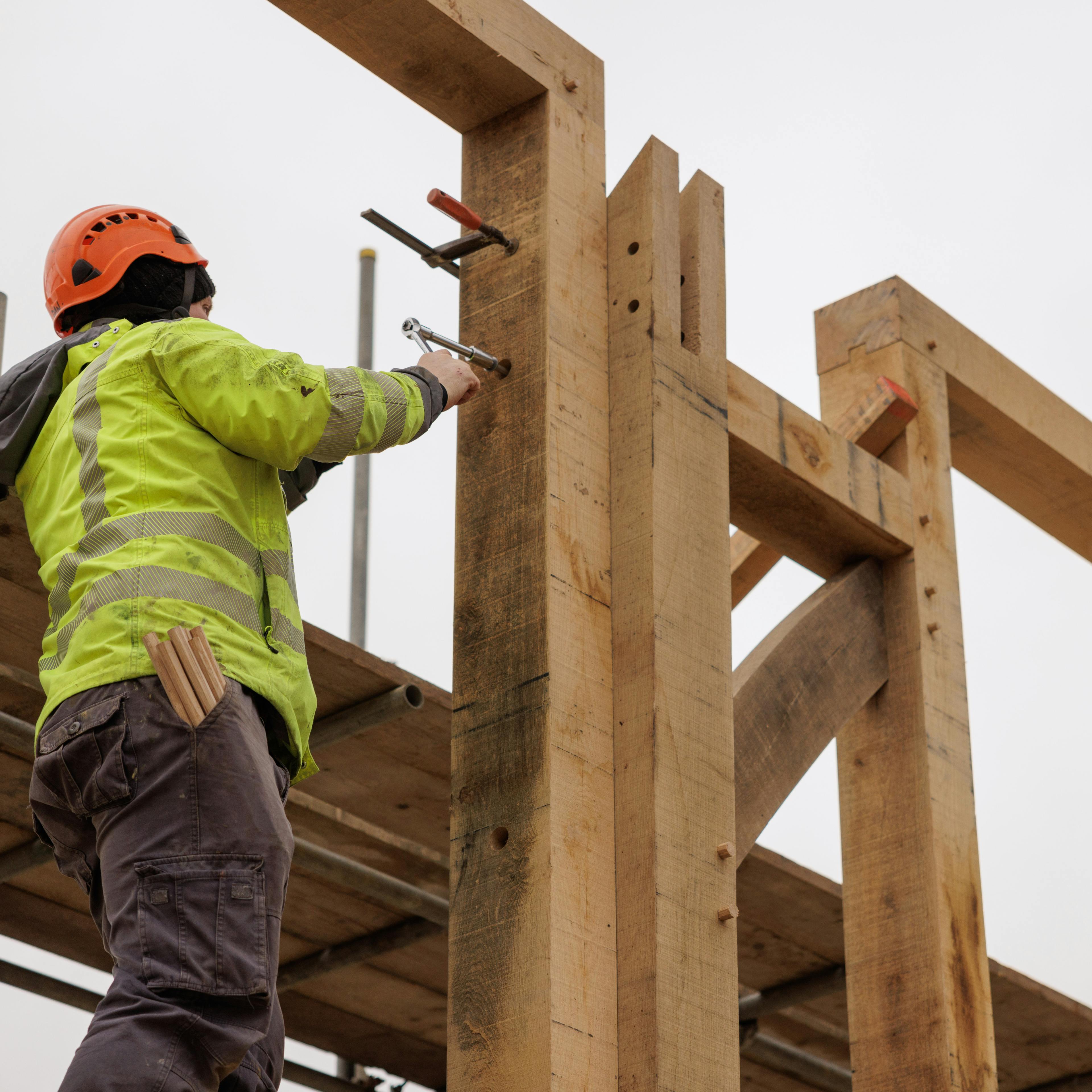 Carpenter carefully installing a section of an oak frame, aligning and securing the timber at a construction site