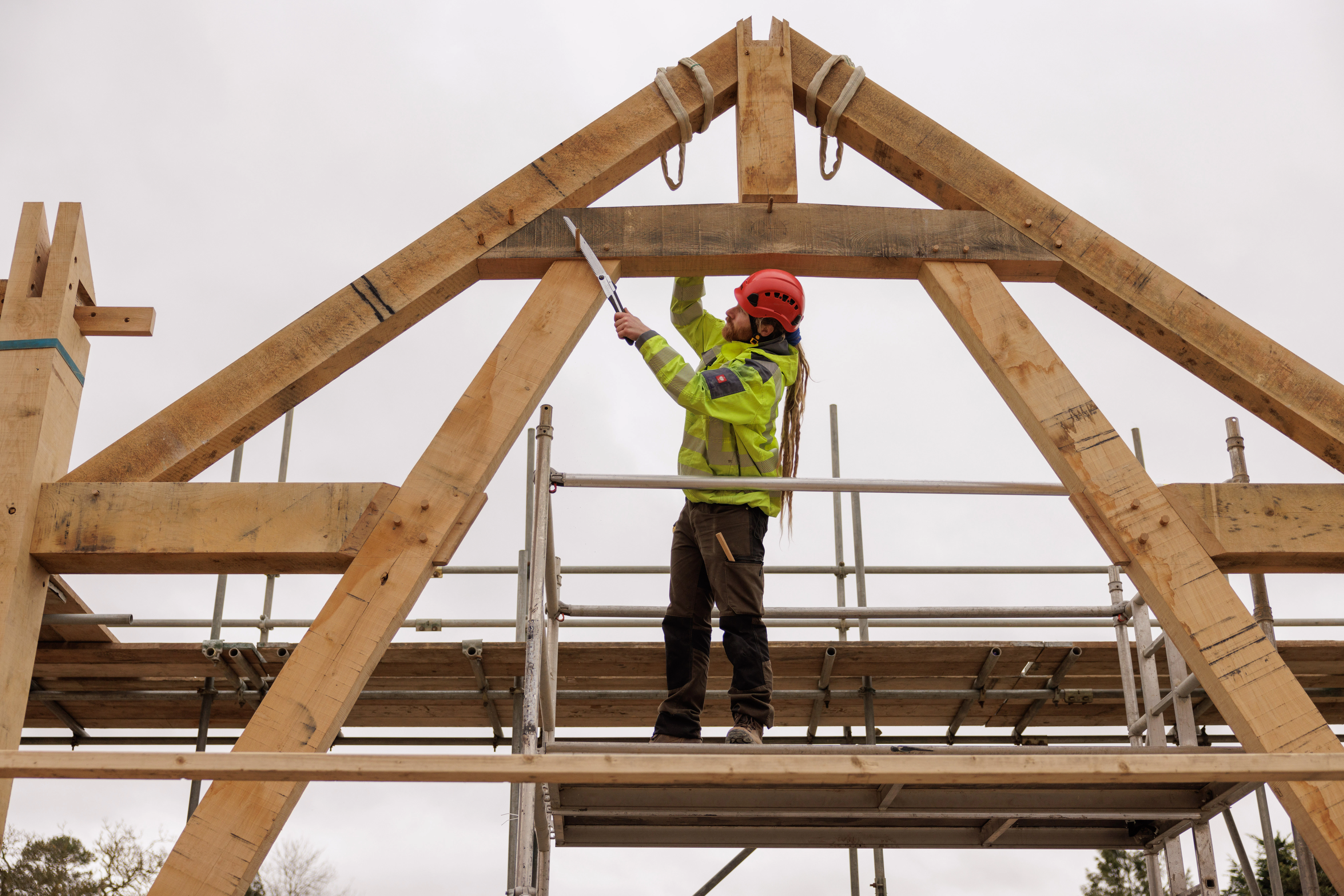Carpenter using a saw to cut wooden pegs on an installed truss at a construction site