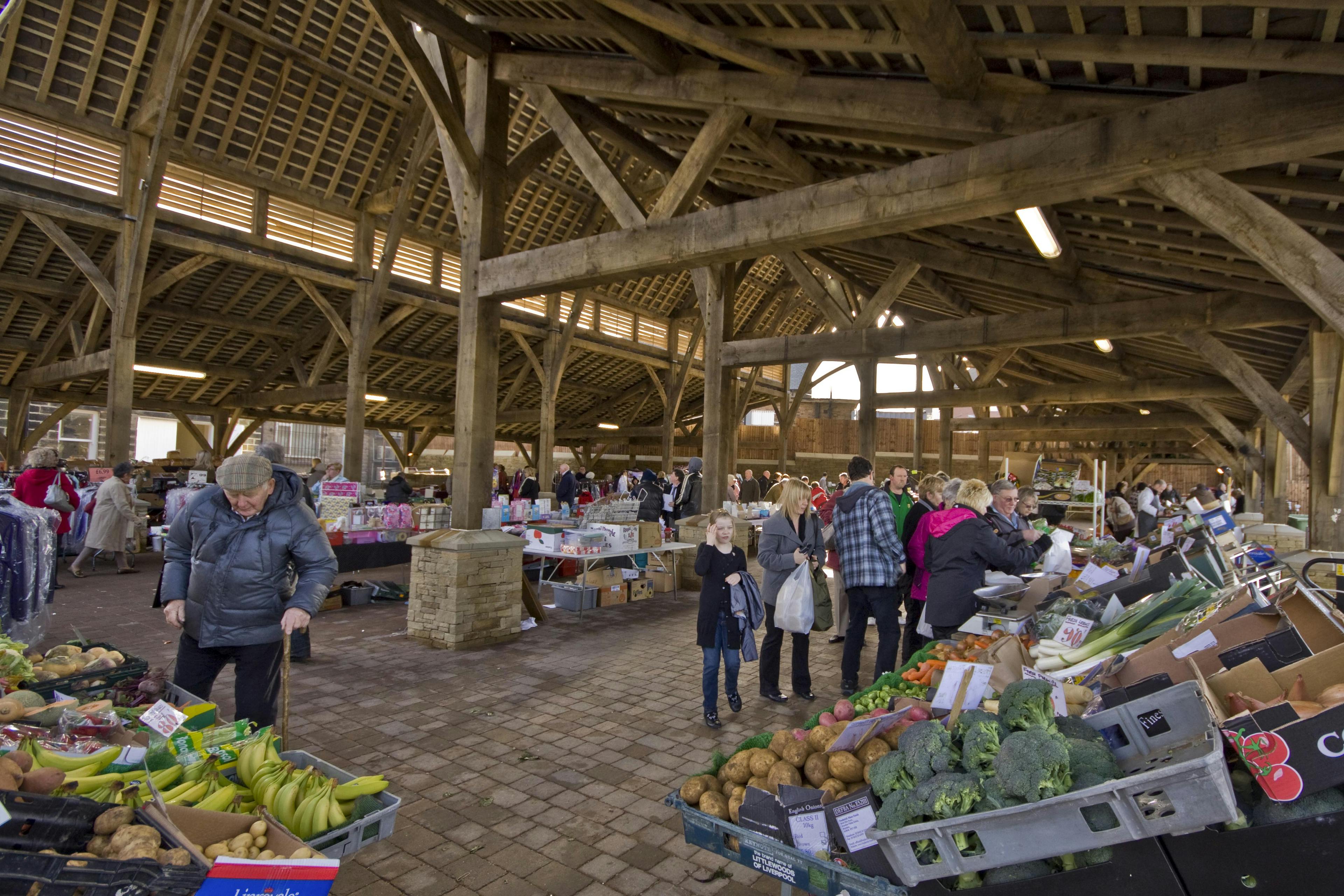 Shoppers browsing stalls inside Penistone Market, surrounded by the traditional green oak frame structure